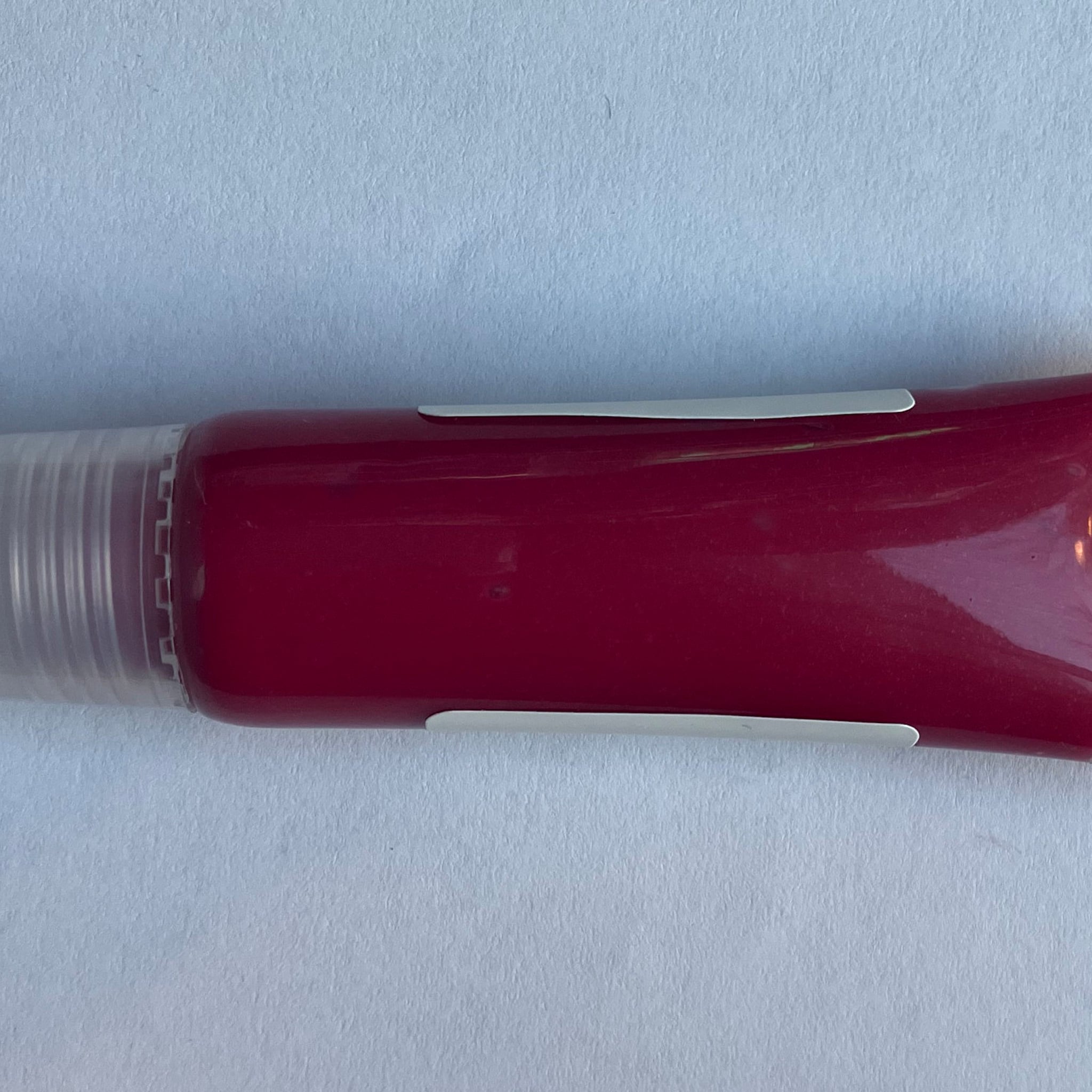 Lip gloss tube with red gloss, white accents, and clear plastic cap on white background