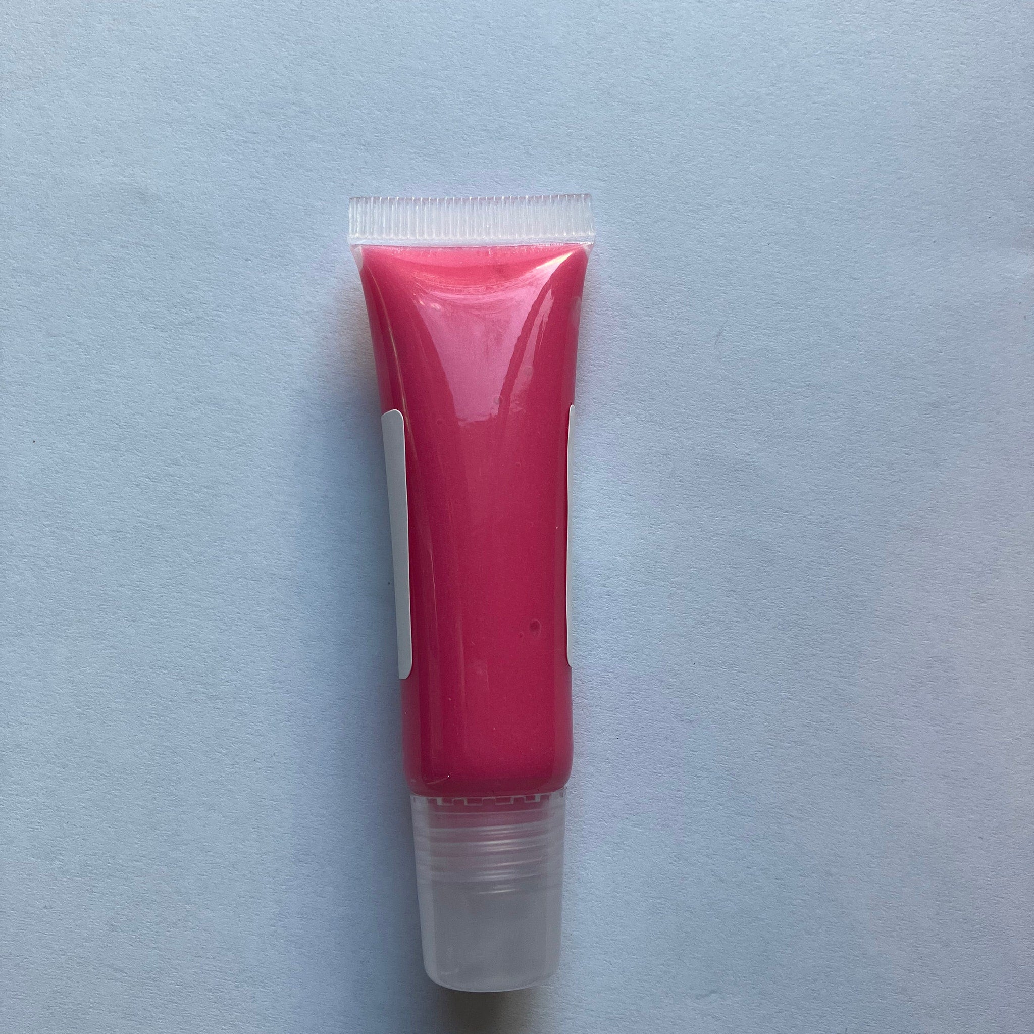 Lip gloss tube with pink liquid, clear applicator, and white label on a light blue background
