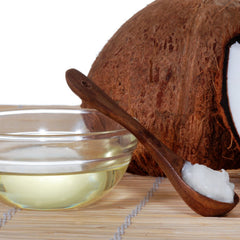 Coconut oil with brown wooden spoon, clear glass bowl, and brown coconut shell on bamboo mat