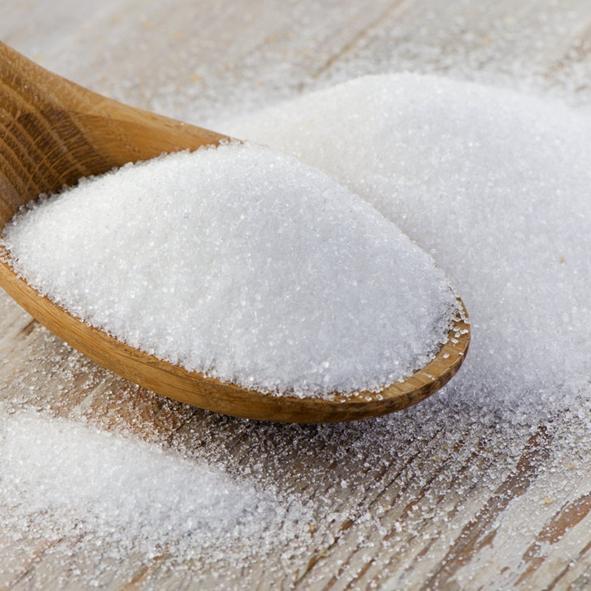 Granulated sugar on wooden spoon with light brown wood grain surface