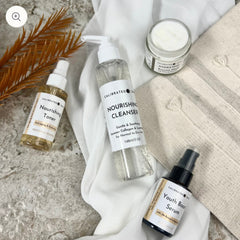 Skincare products on white fabric, including clear cleanser, yellow toner, and black serum bottles with labels