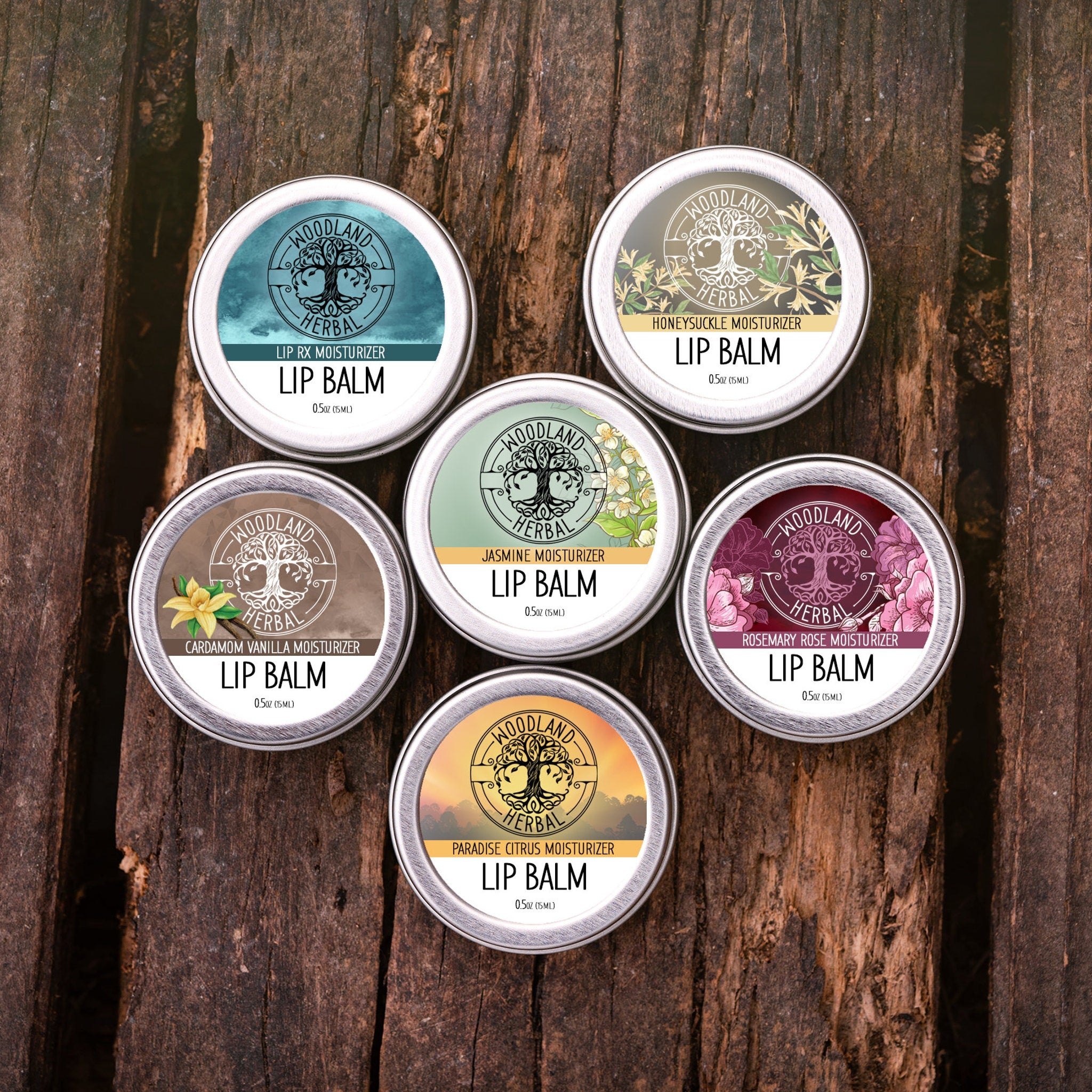 Lip balm tins with Woodland Herbal logo, various colors and floral designs, on wood surface