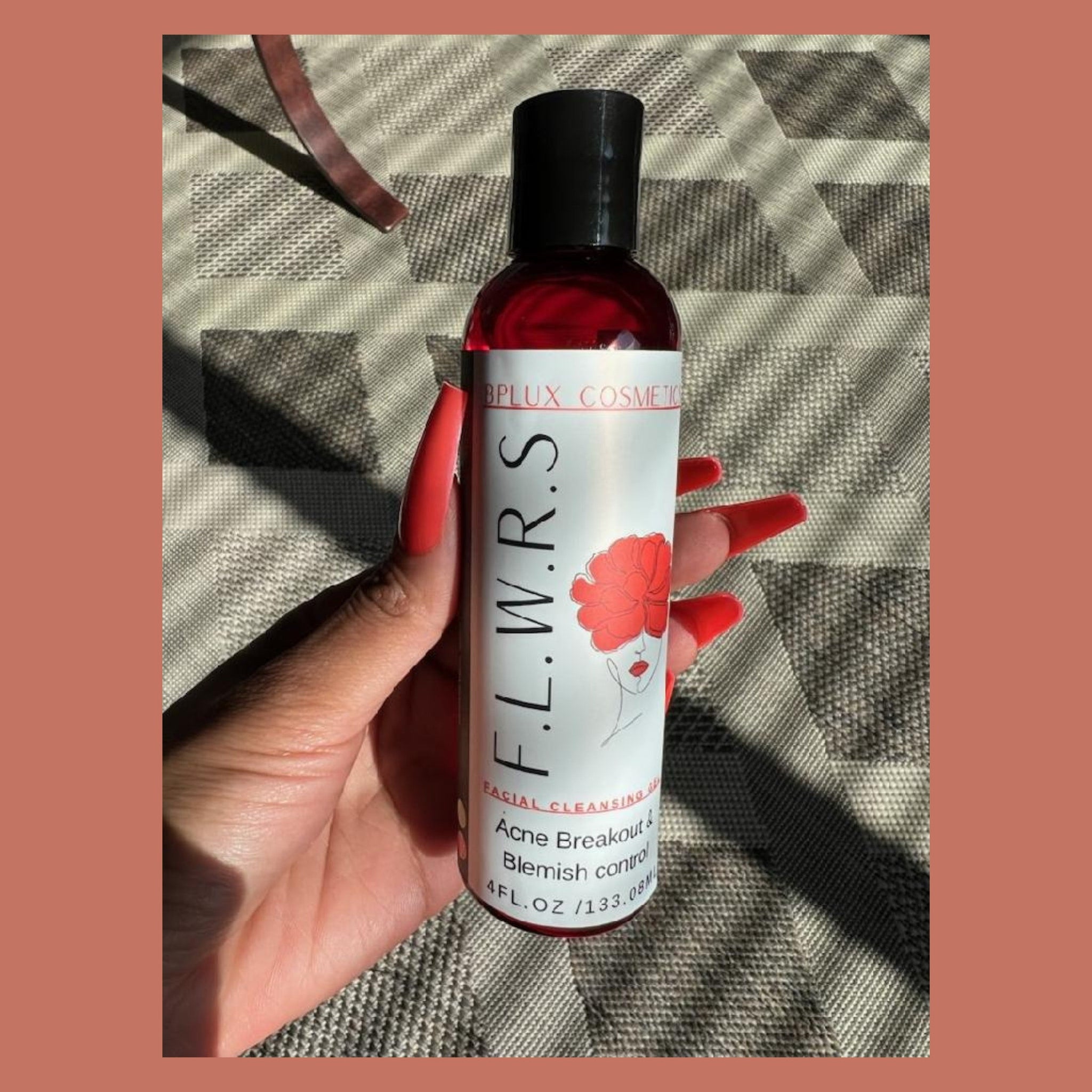 Facial cleanser bottle with red liquid, black cap, and white label held by hand with red nails