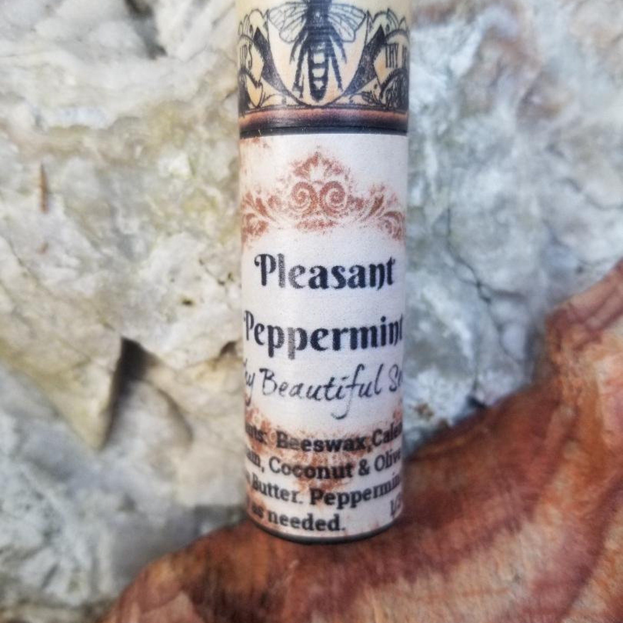 Peppermint lip balm tube with white and brown label, bee illustration, and script text on a textured background