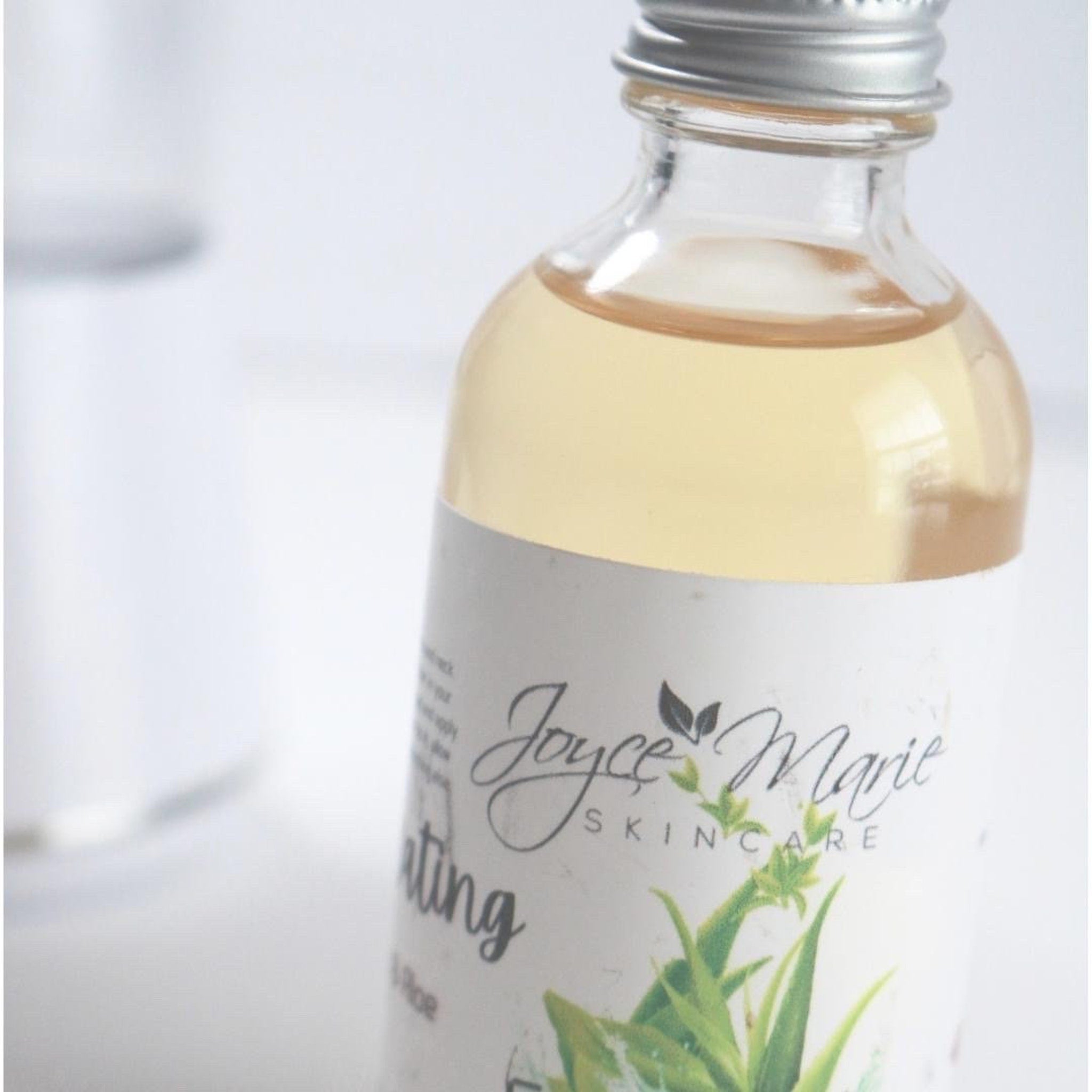 Skincare bottle with clear glass, silver cap, and Joyce Marie label