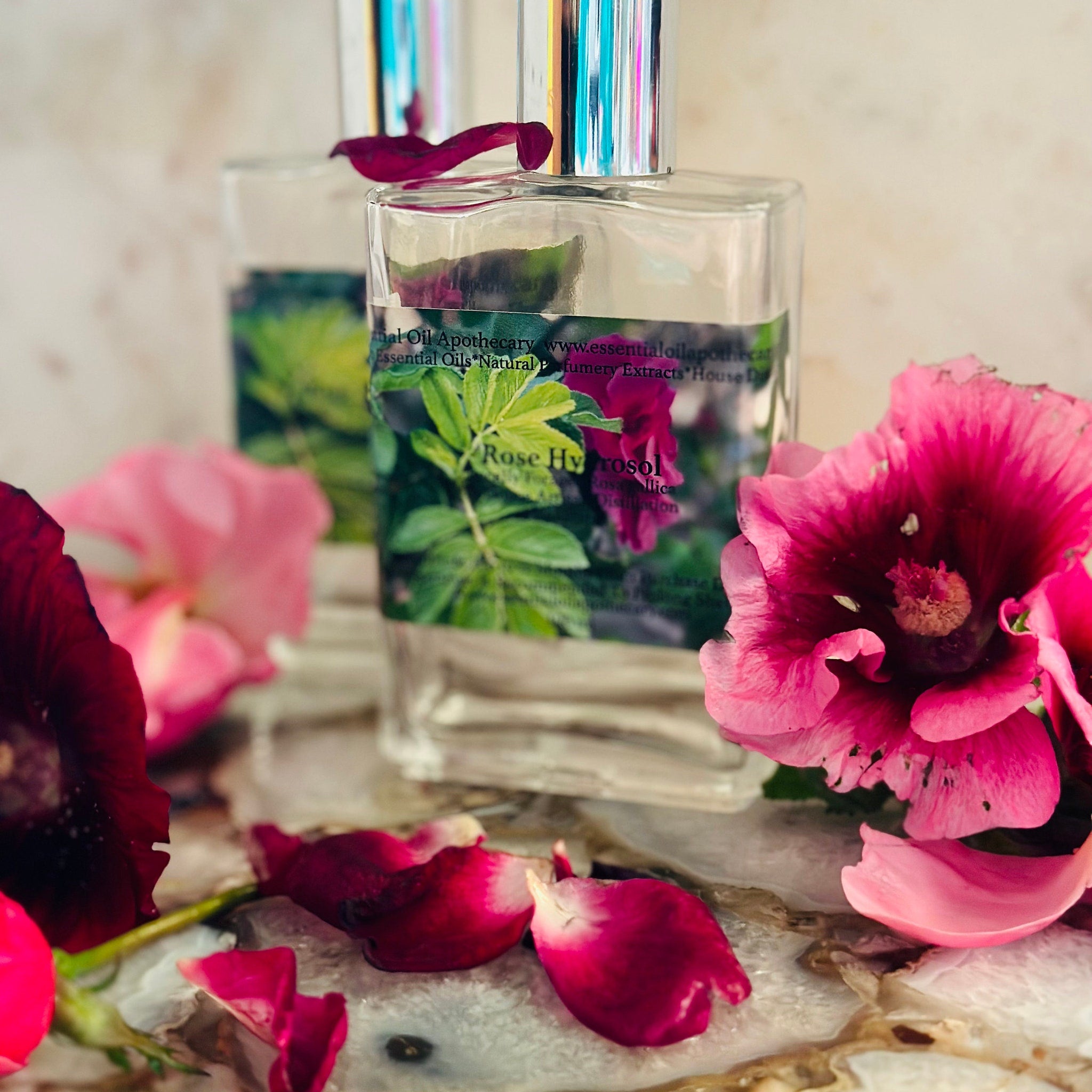 Essential oil bottles with silver caps, clear glass, and floral label, surrounded by pink and red flower petals