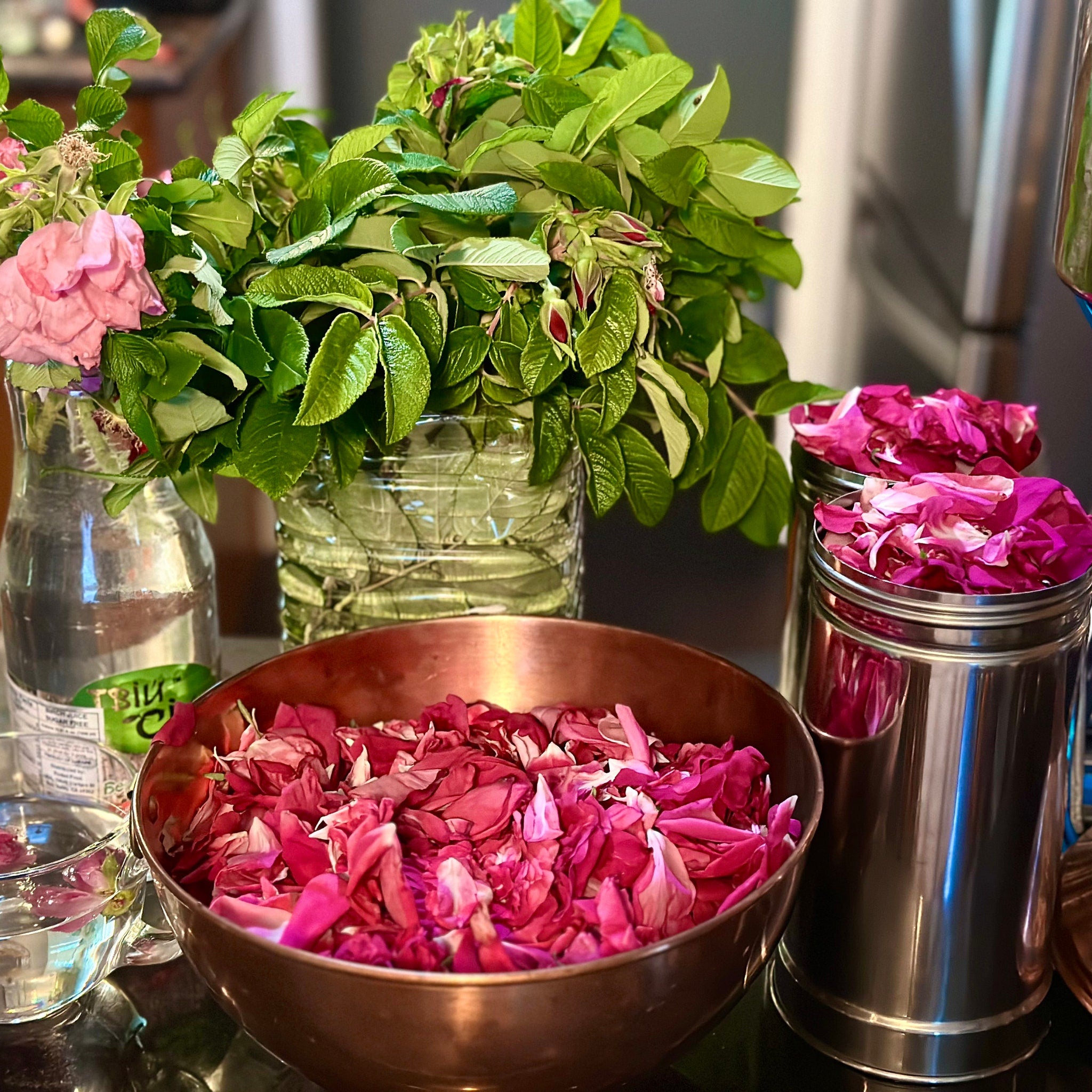 Rose petals in a copper bowl with pink petals and green leaves in glass vases