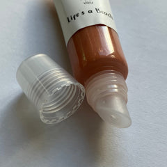 Lip gloss tube with clear plastic cap, brown gloss, and "Life's a Beach" text from Glossy New You brand