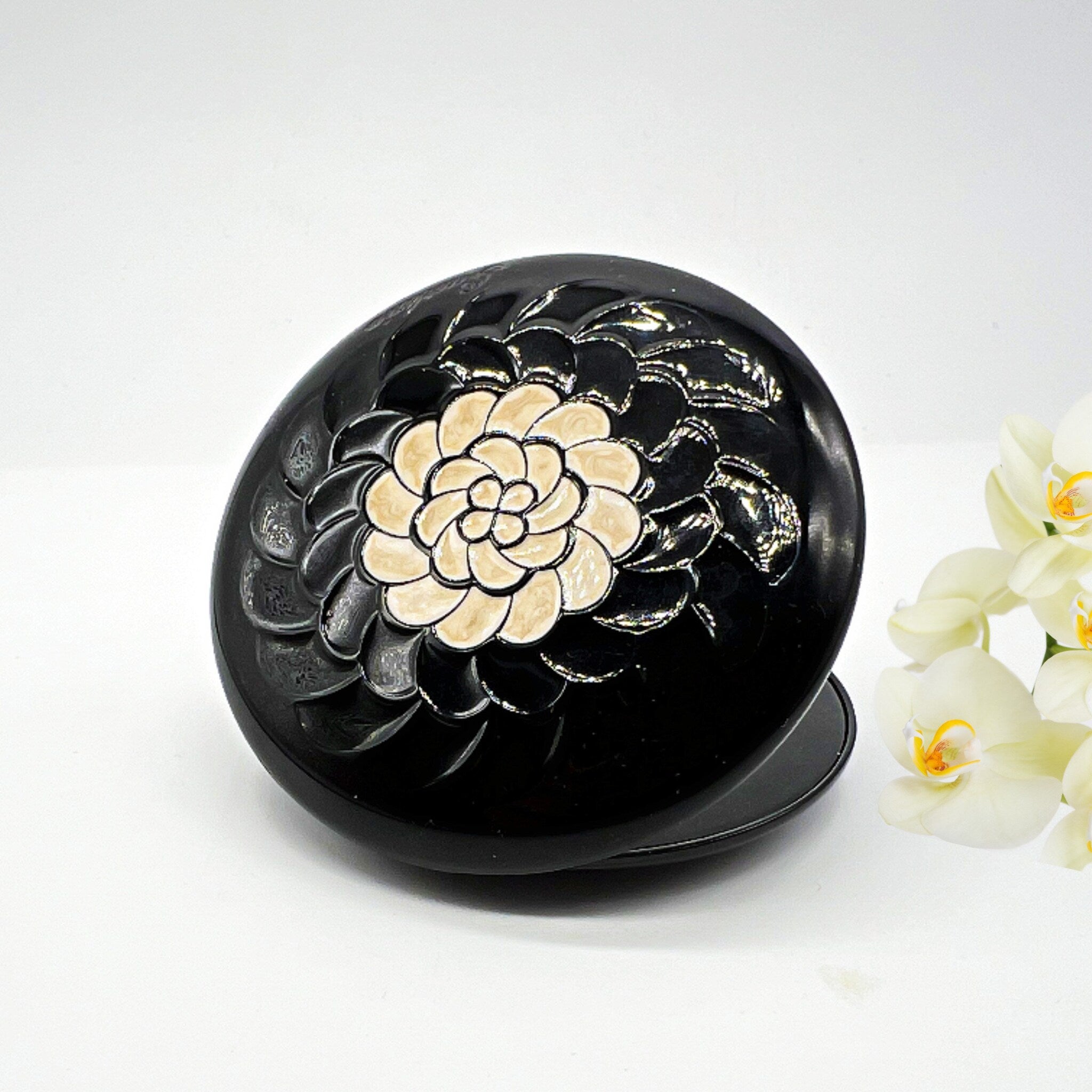 Black compact with floral design and beige center detail, on white surface