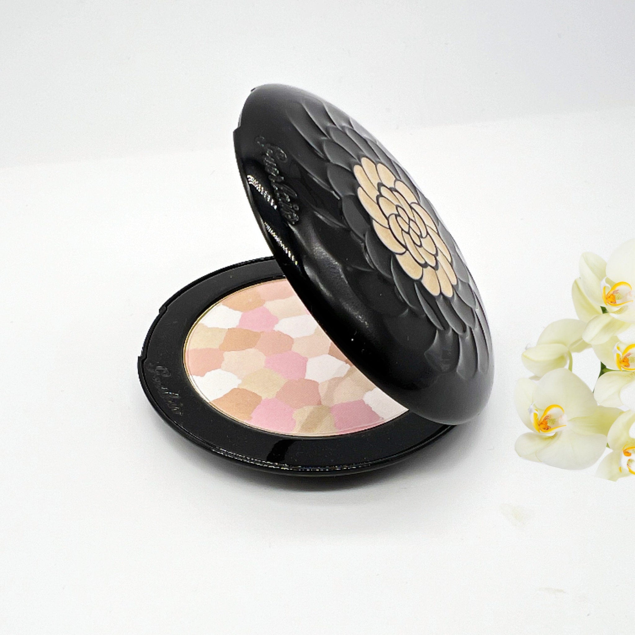 Powder compact with black floral design, multi-colored powder, and brand text visible