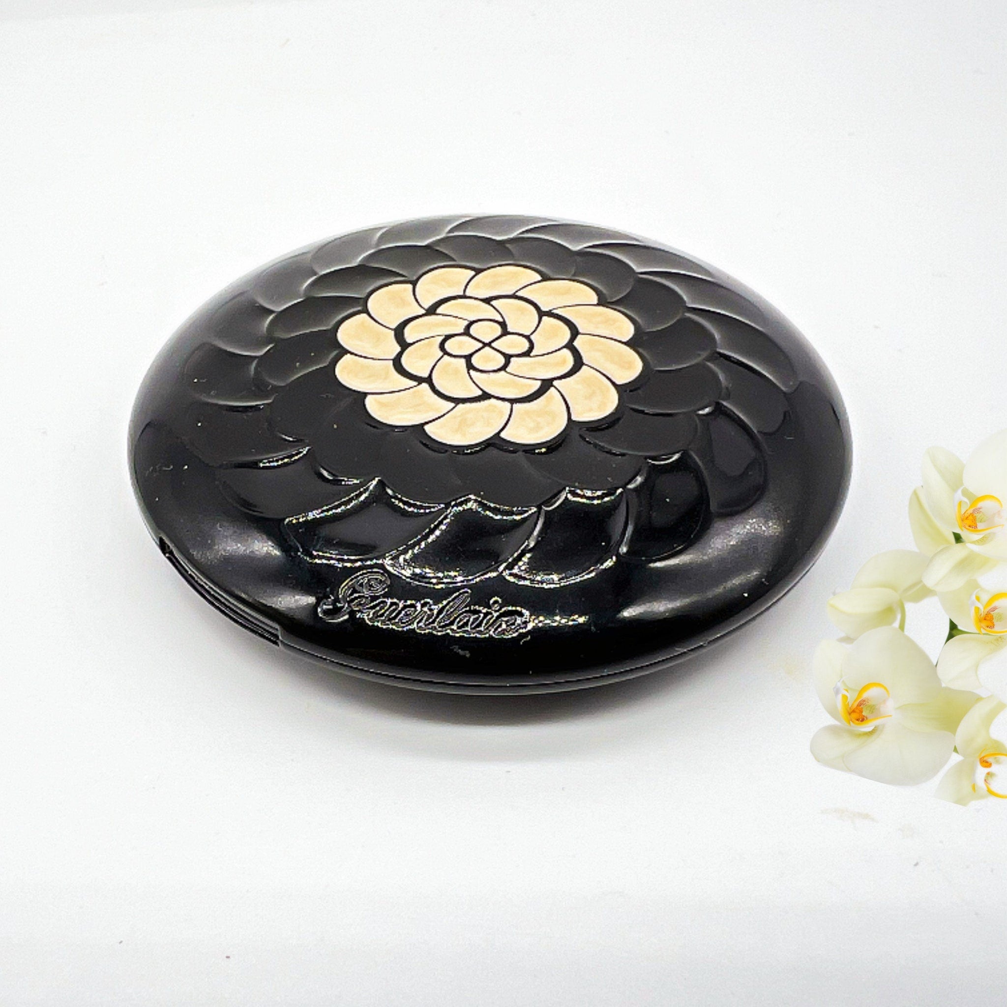 Compact powder with black floral design, gold accents, and Guerlain brand text visible