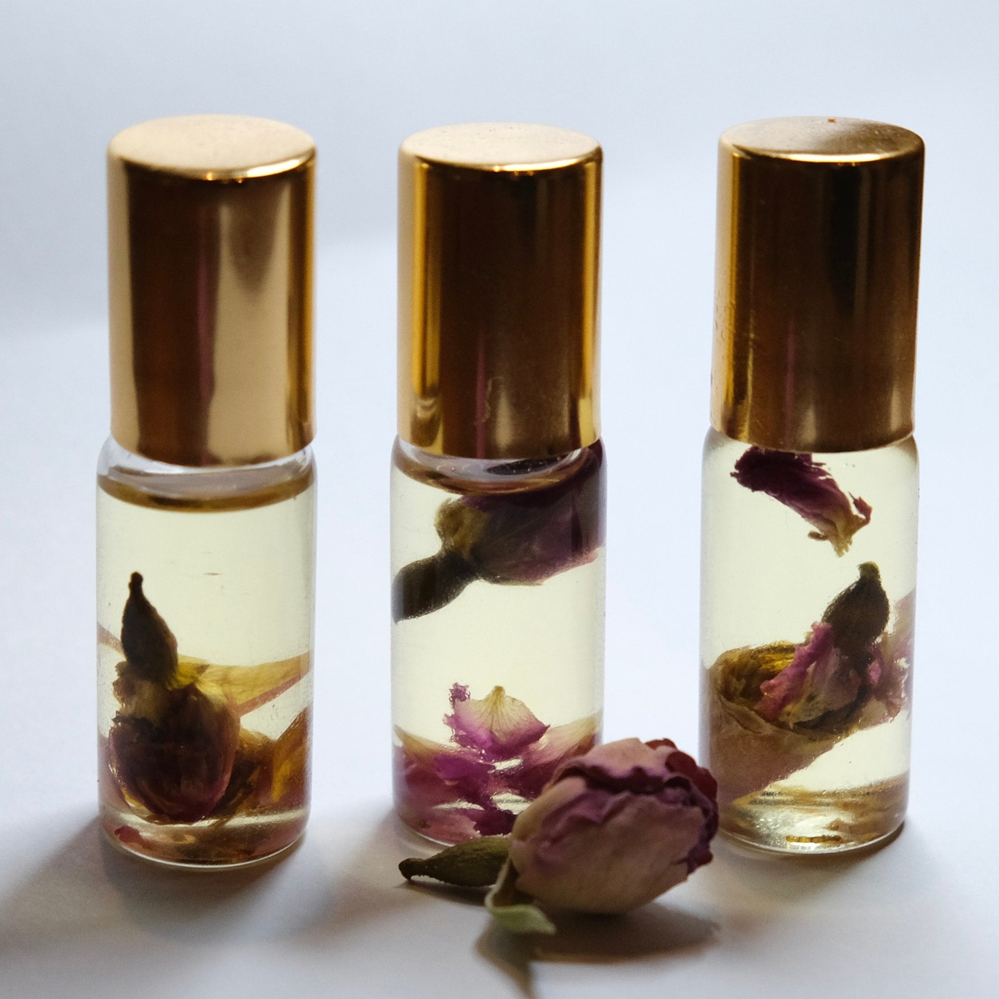 Essential oil bottles with gold caps, clear glass, and dried rose petals inside