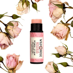 Lip balm tube with pink label, black cap, surrounded by dried pink roses and buds, Wild Rose brand