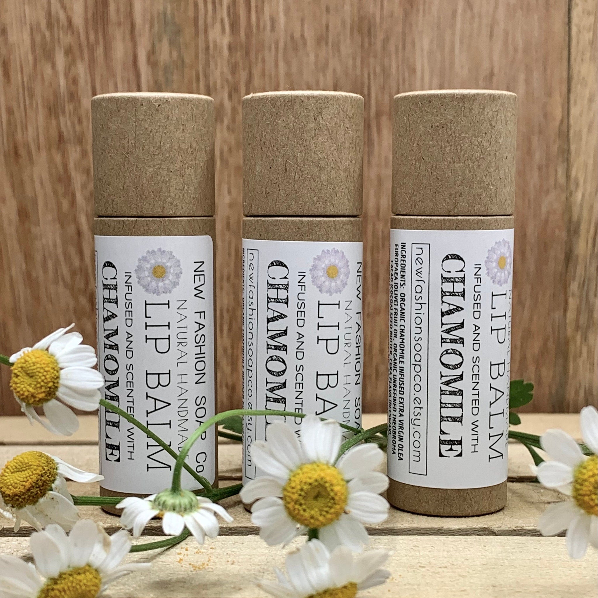 Lip balm tubes in brown cardboard with white labels, chamomile flowers, and newfashionsoapco text