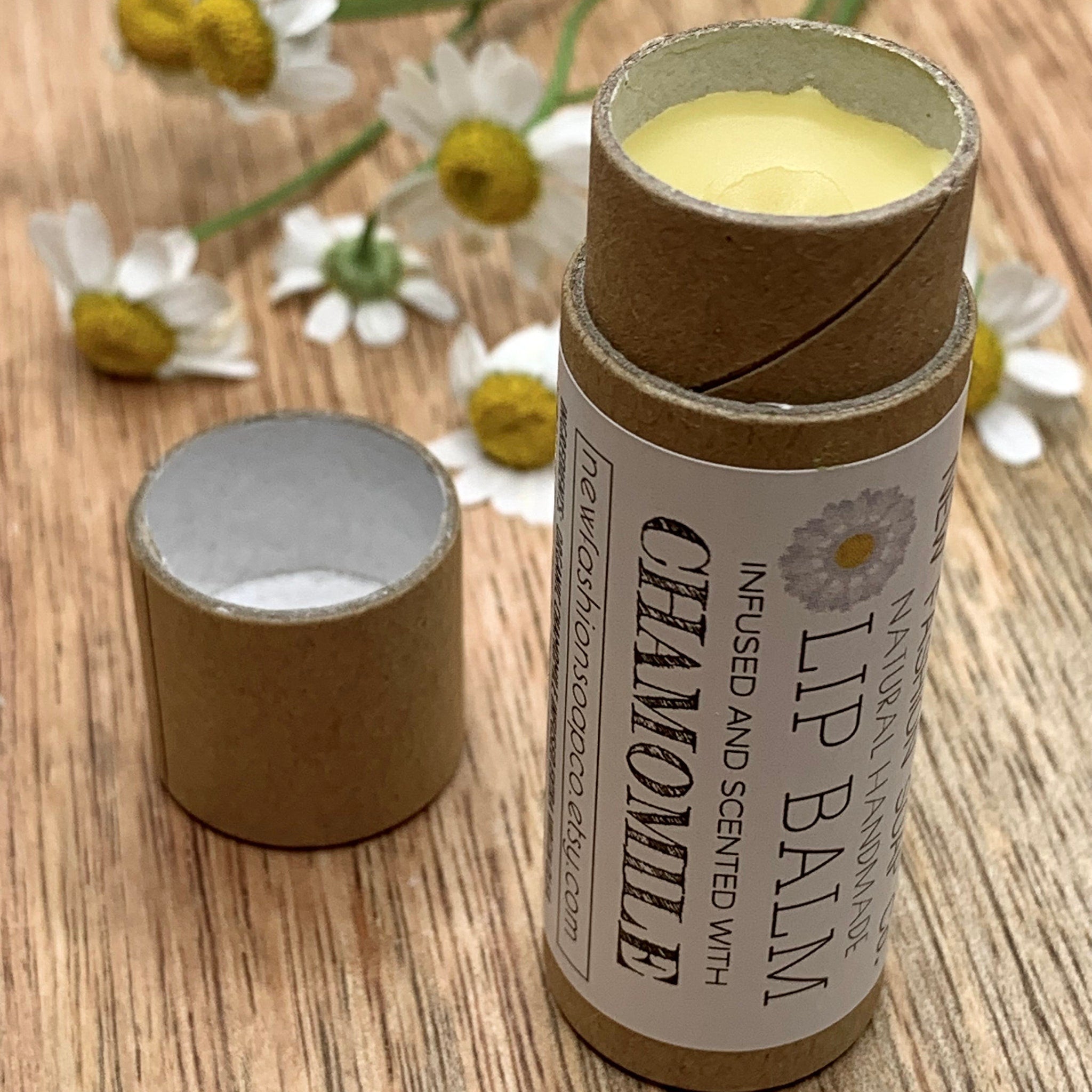 Lip balm in brown cardboard tube with yellow balm and "Chamomile" label, on wood surface