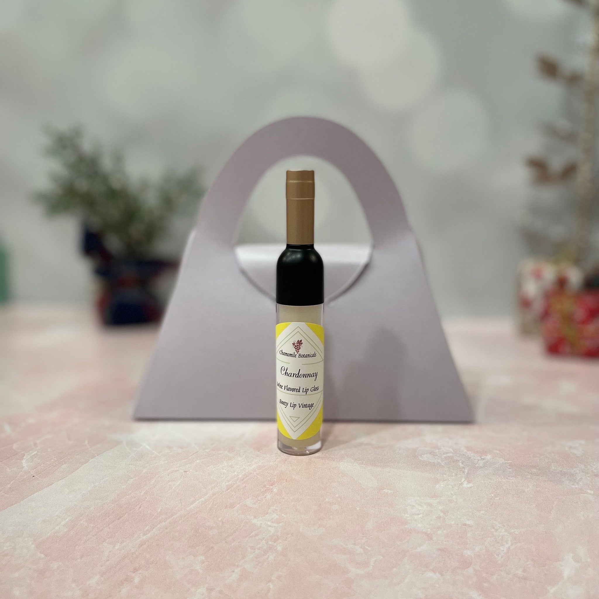 Lip gloss bottle with black, gold, and yellow label, Chamomile Botanicals branding visible, presented as a gift