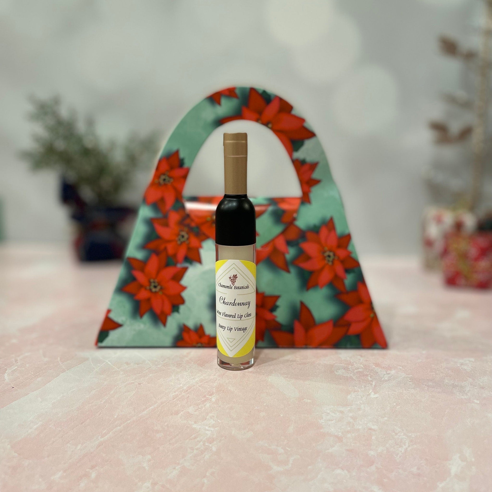 Lip gloss bottle with black cap, yellow label, and floral gift bag in background