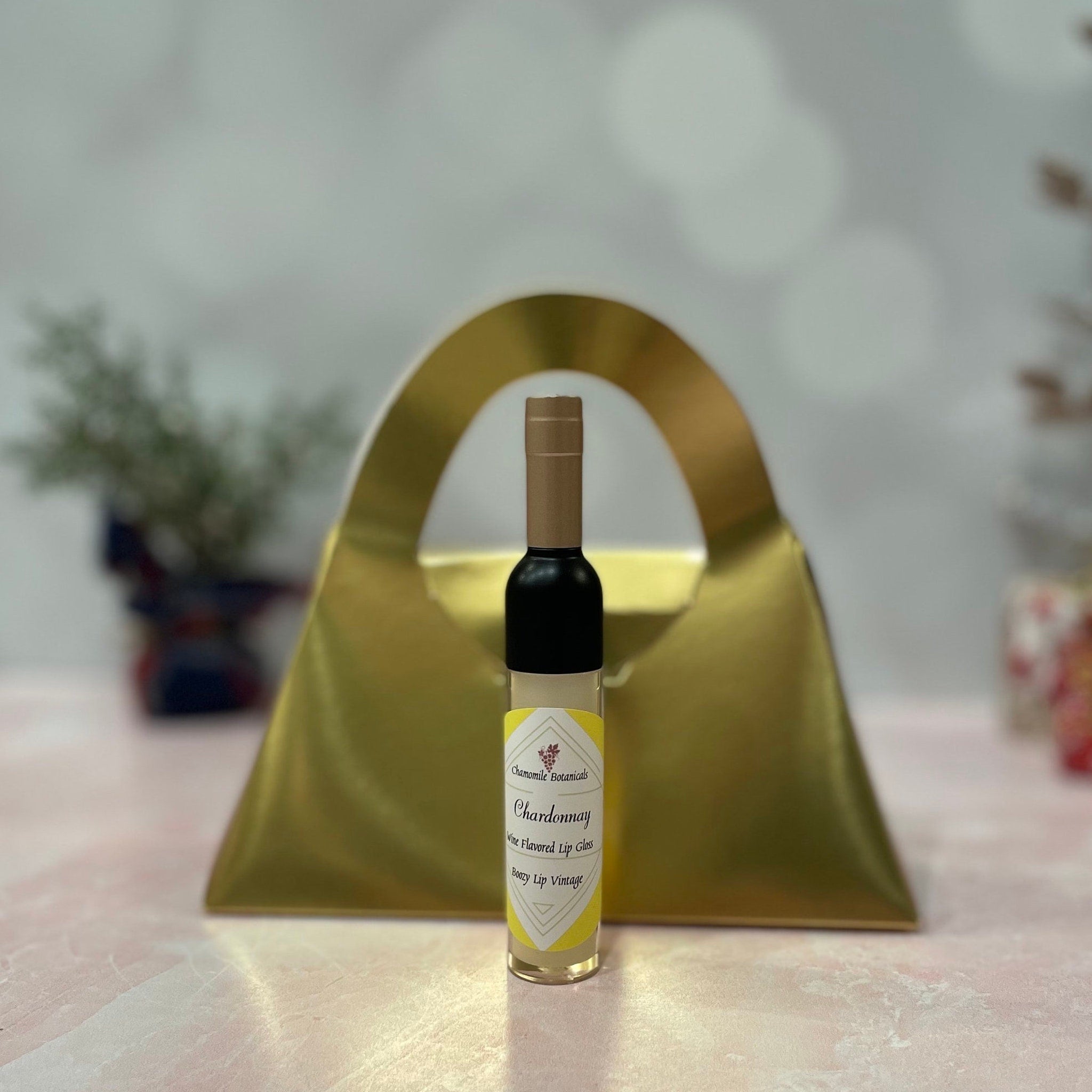 Lip gloss bottle with black and gold cap, yellow label, and gold background, Chamomile Botanicals text
