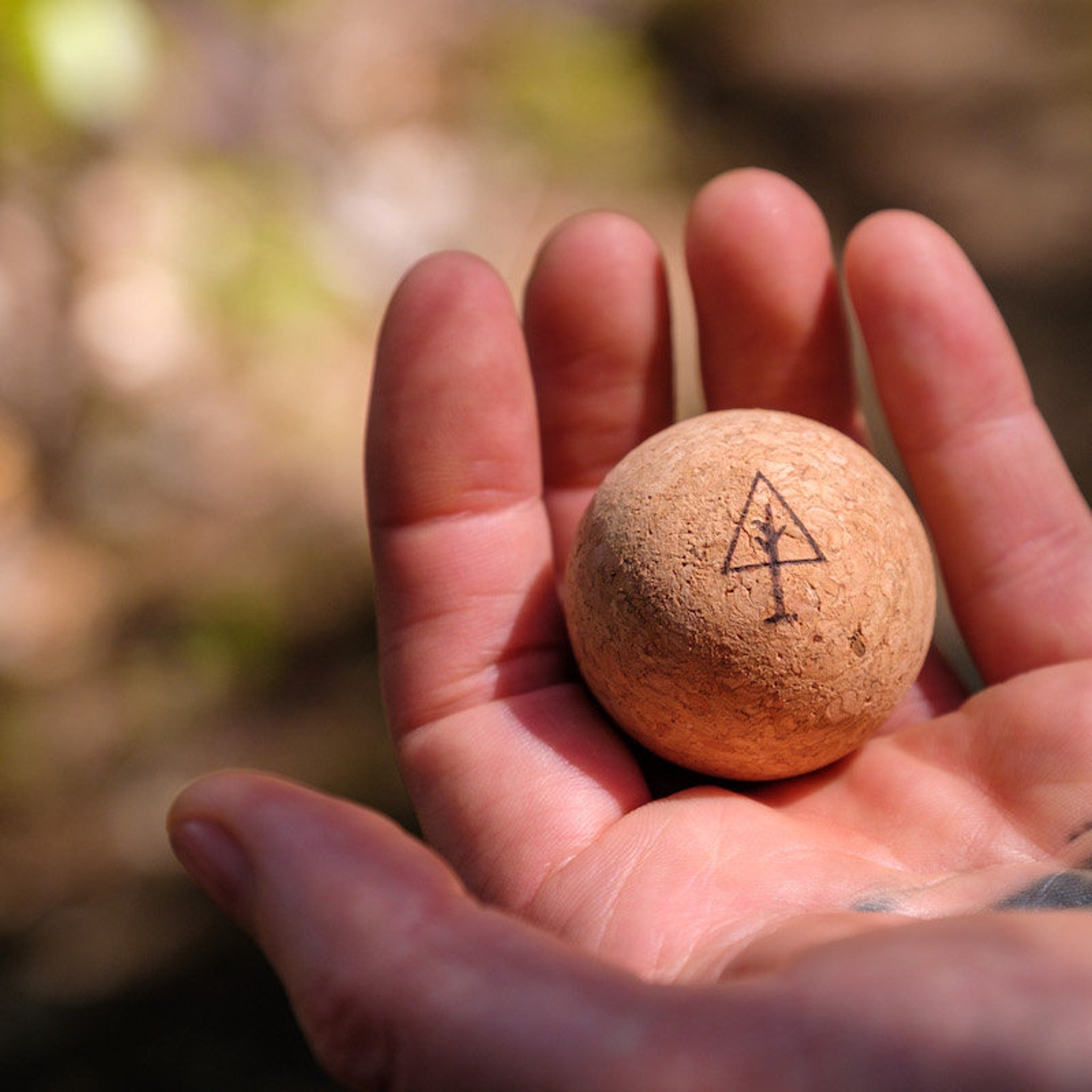 Cork ball with tree logo, held in hand, natural cork material, black logo detail