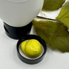 Yellow cream in black container with white bottle and green leaf background