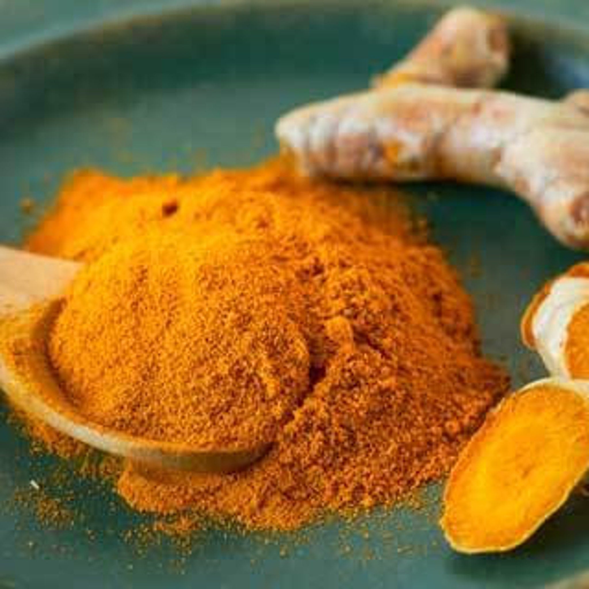 Turmeric powder with orange color and wooden spoon on a green plate
