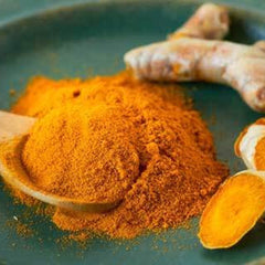 Turmeric powder with orange color and wooden spoon on a green plate