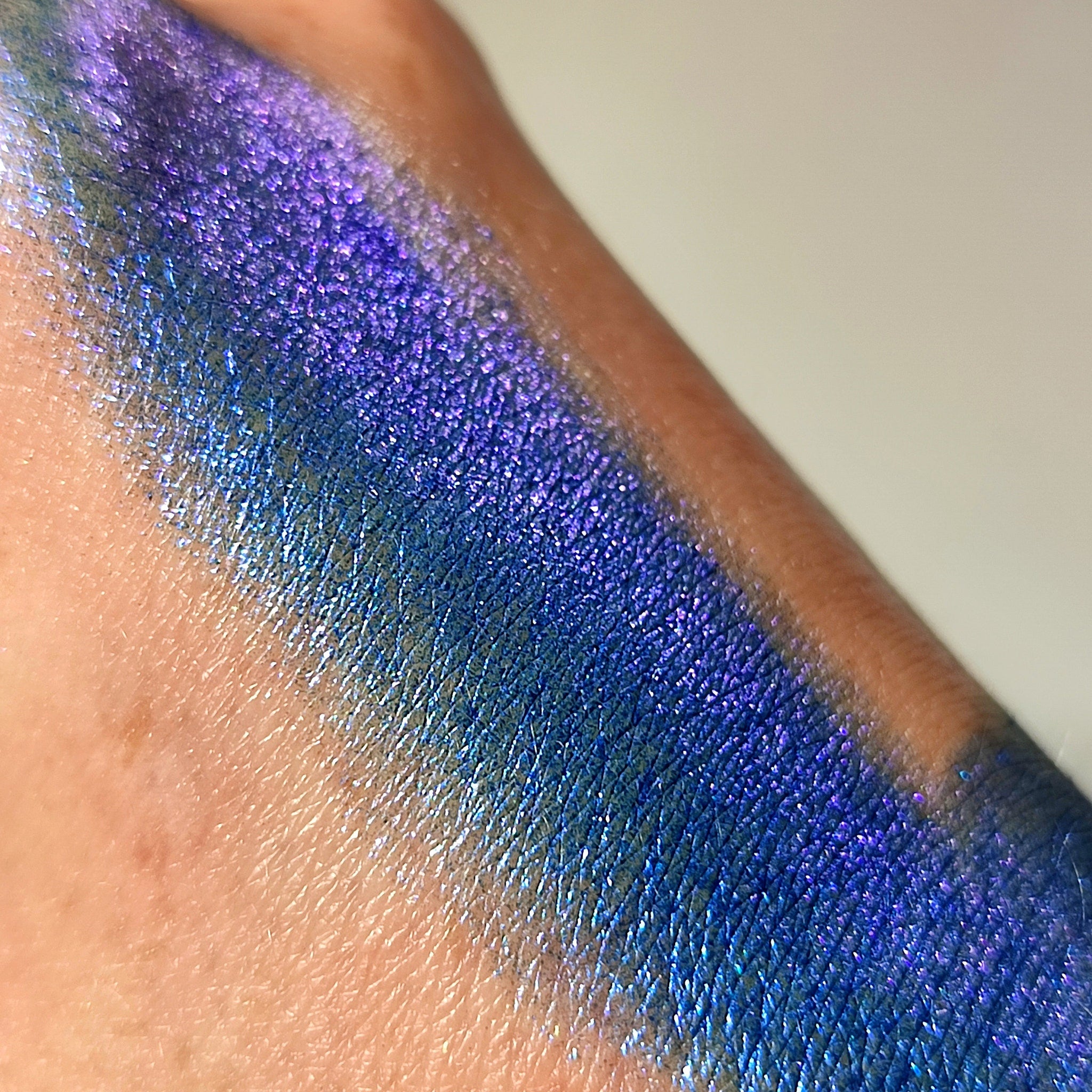 Glitter eyeshadow swatch in blue and purple, applied on skin, showing shimmer effect
