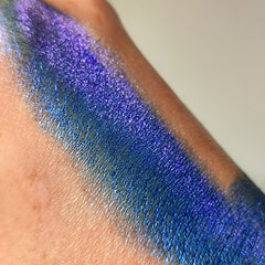 Glitter eyeshadow swatch in blue and purple, applied on skin, showing shimmer effect