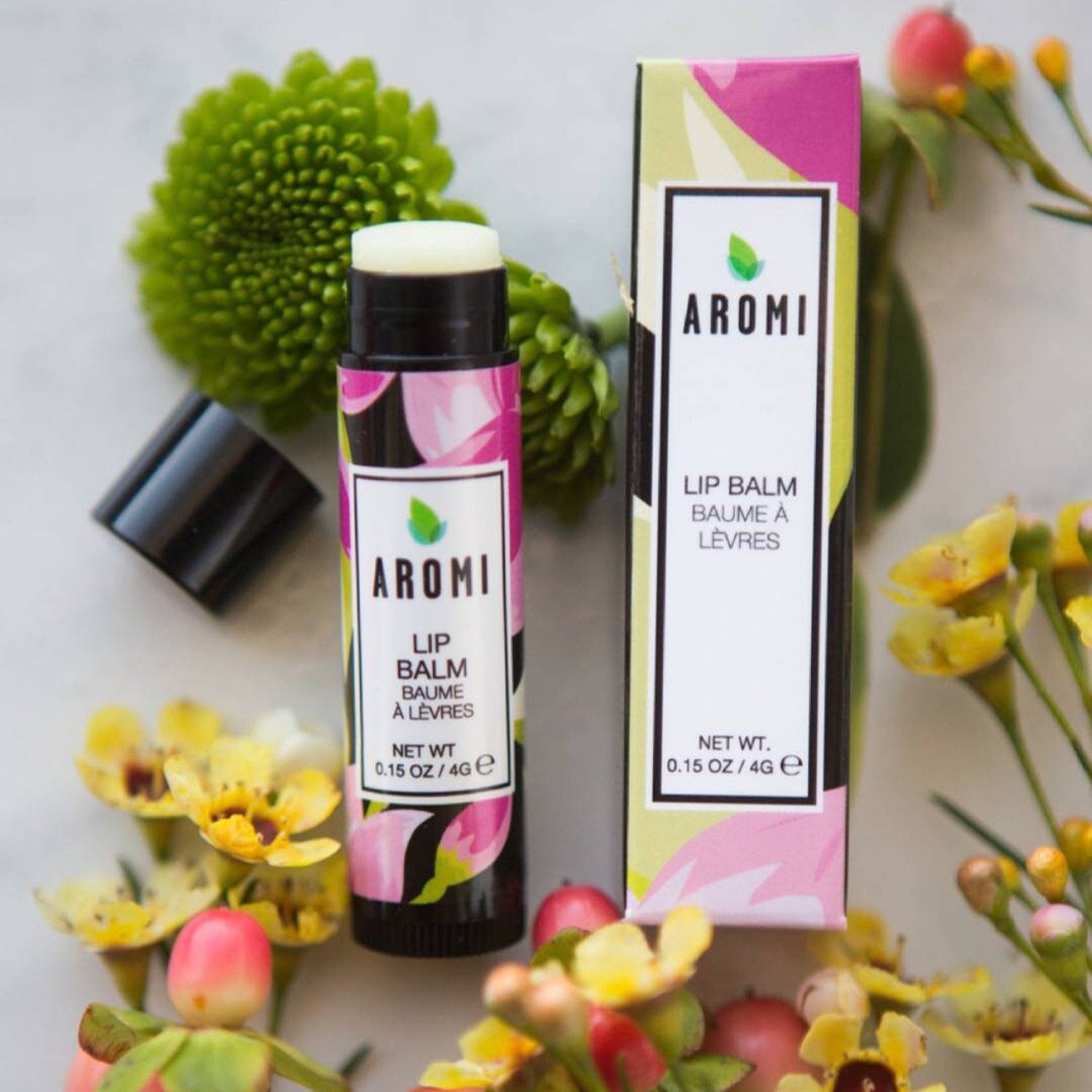 Lip balm tube with floral pattern and Aromi brand name, with box and flowers around it