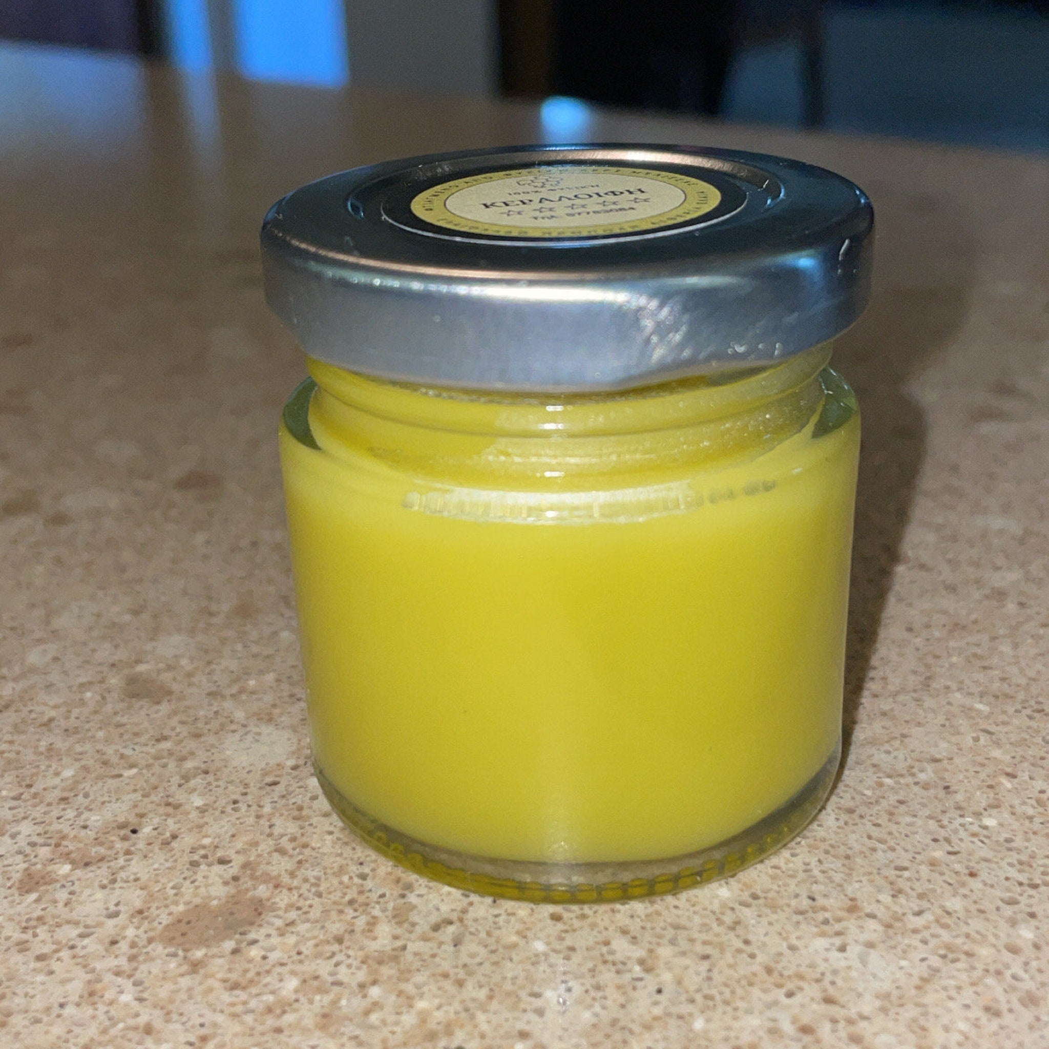 Jar of yellow liquid in glass container with silver lid, text label visible on top