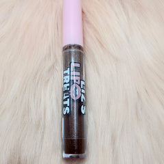 Lip gloss tube with pink cap and brown glitter, "Lips Treats" label on a furry background.