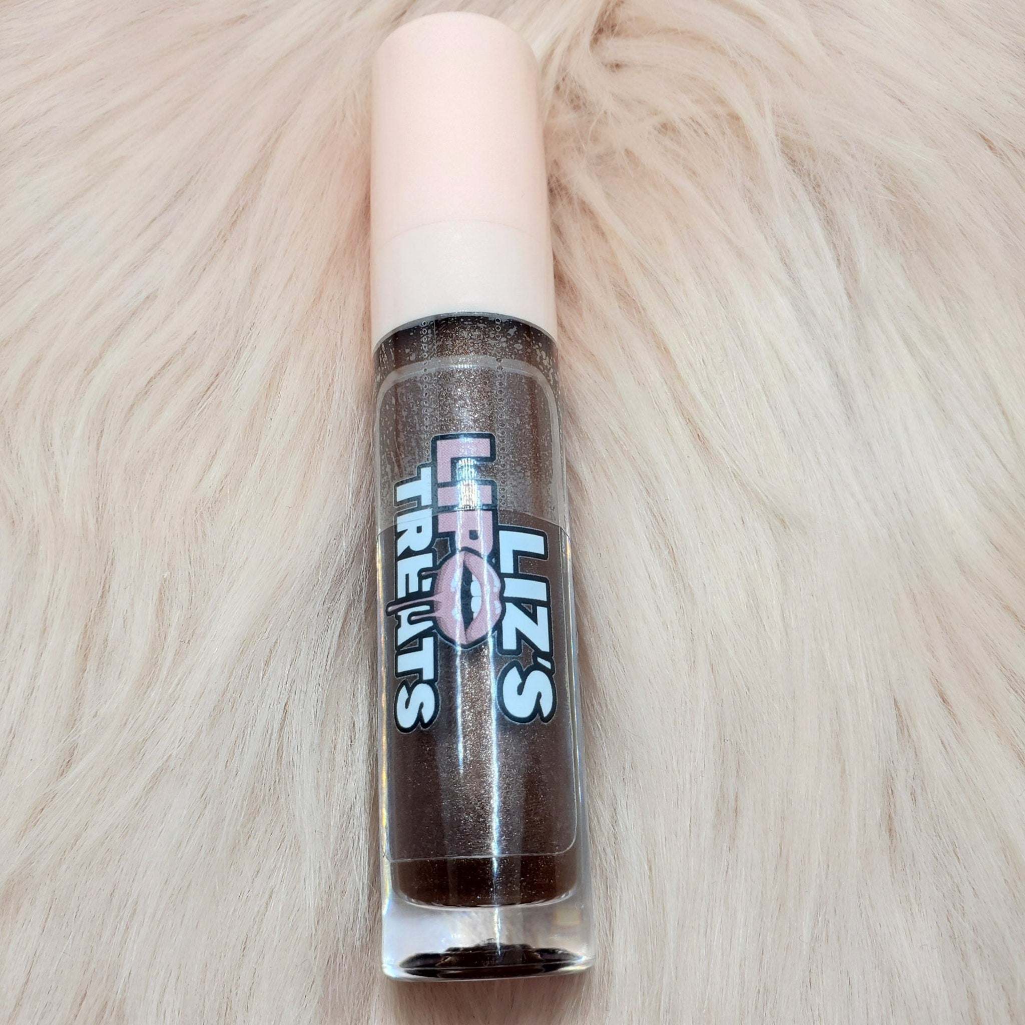 Lip gloss tube with brown glitter, pink cap, and "Liz's Treats" label on a fluffy white surface