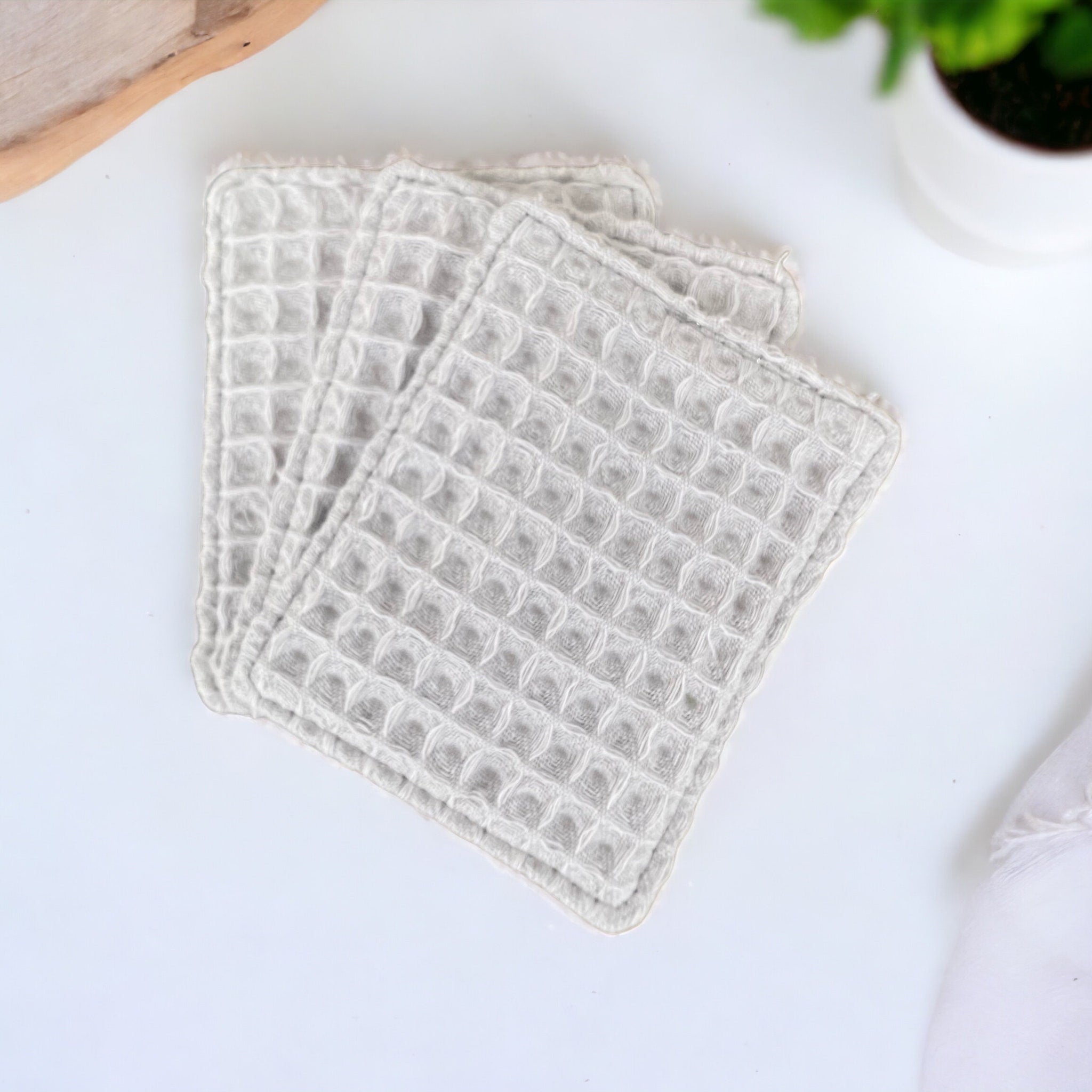 Reusable face cloths in light grey waffle weave fabric, stacked on white surface