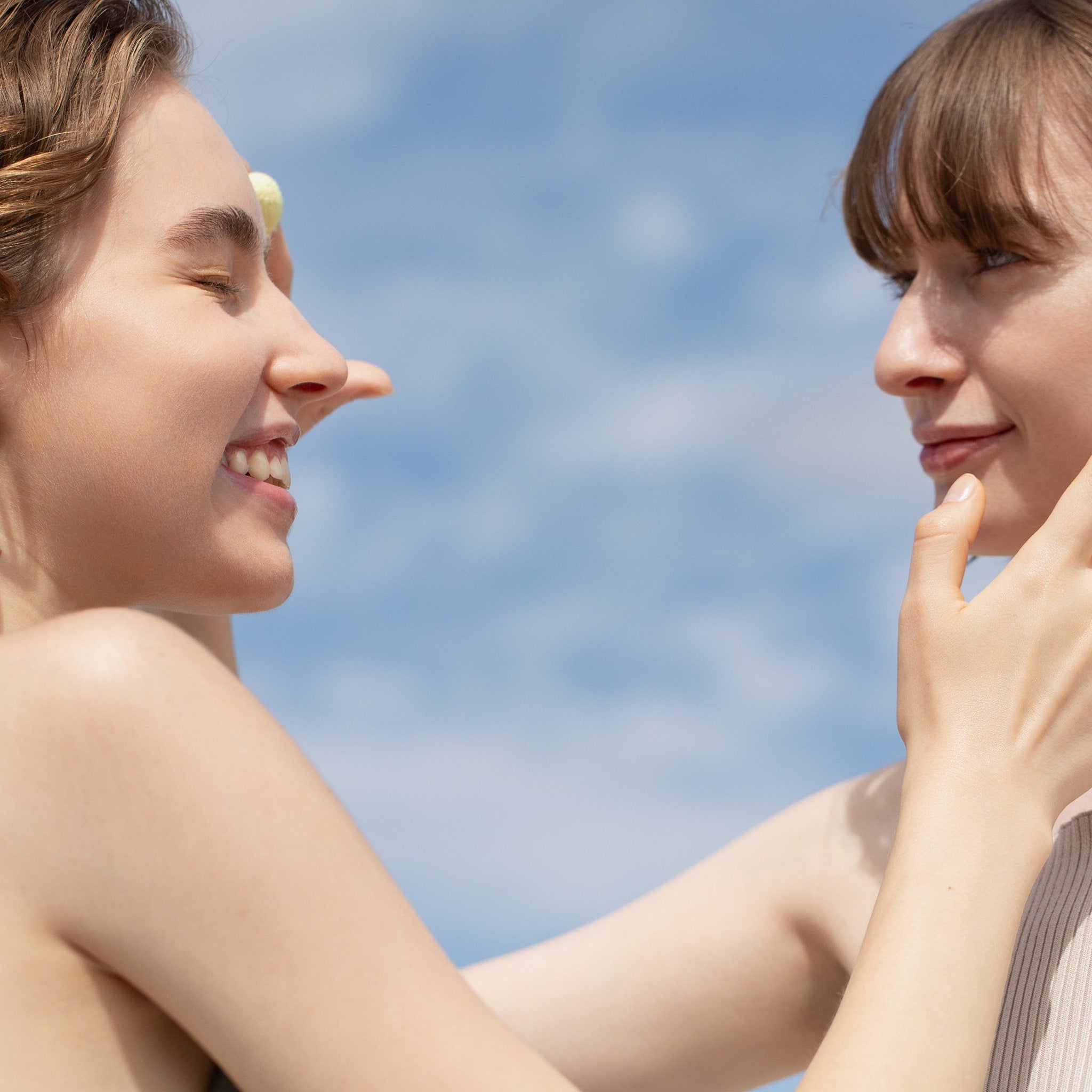 Two women smiling, fair skin, light brown hair, blue sky background