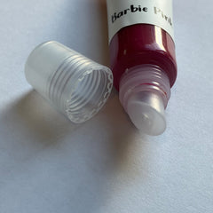 Lip product tube with clear plastic cap, dark pink liquid, and "Barbie Pink" label text