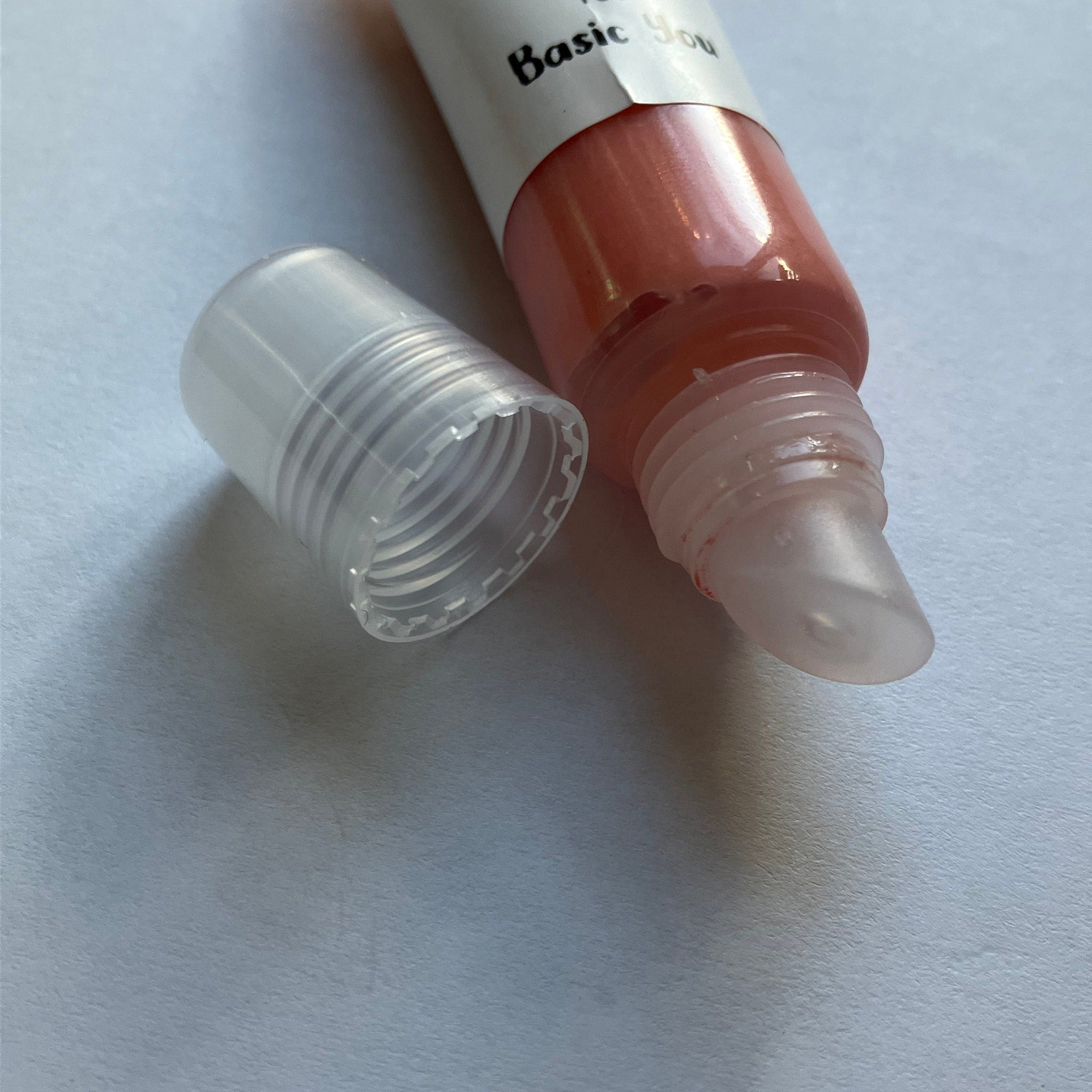 Lip gloss tube with clear cap, peach-colored gloss, and "Basic You" label visible
