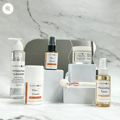 Skincare products set with white, clear, and gold bottles on white blocks and marble background