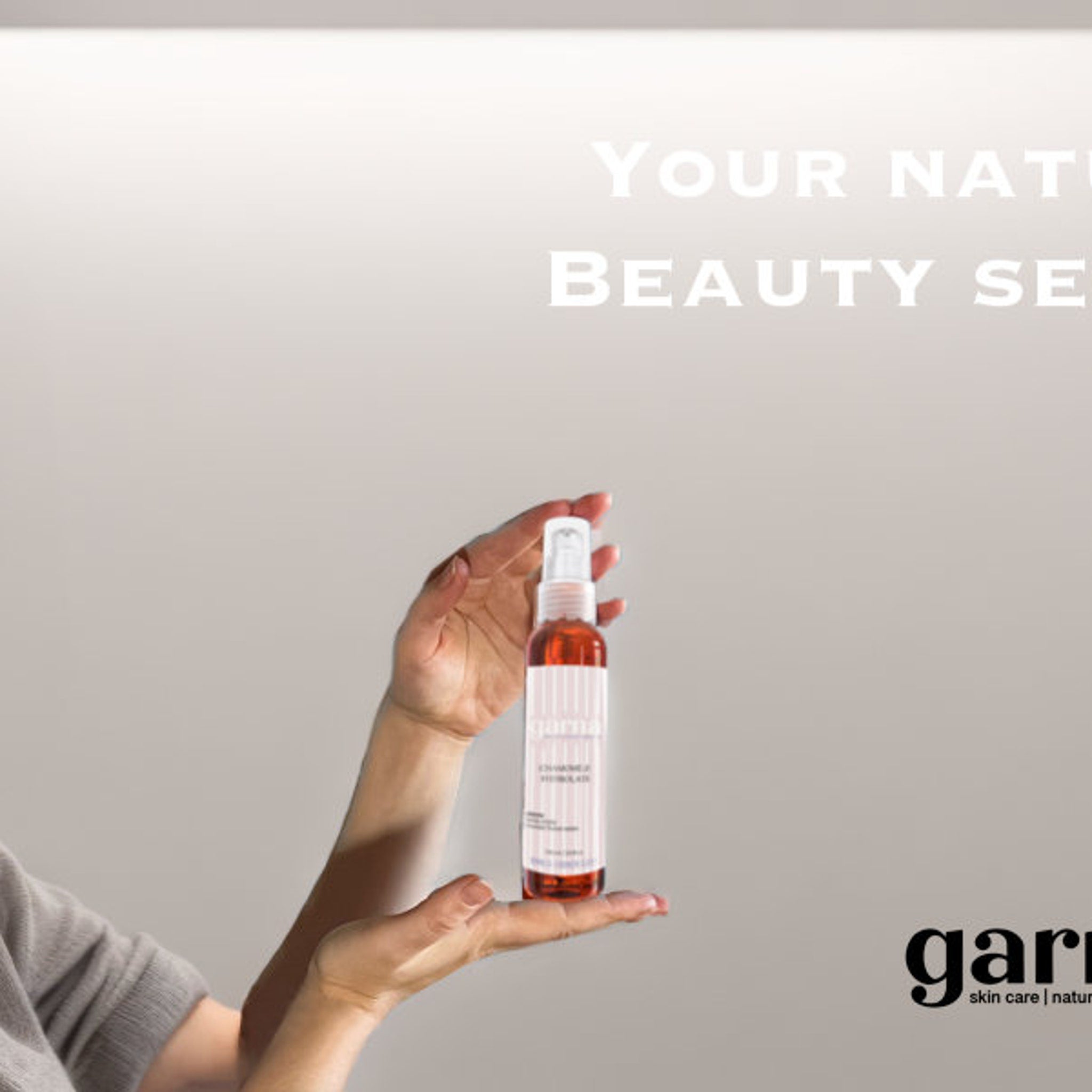 Spray bottle with clear and white dispenser, orange liquid, held in hand by "garna" skin care.