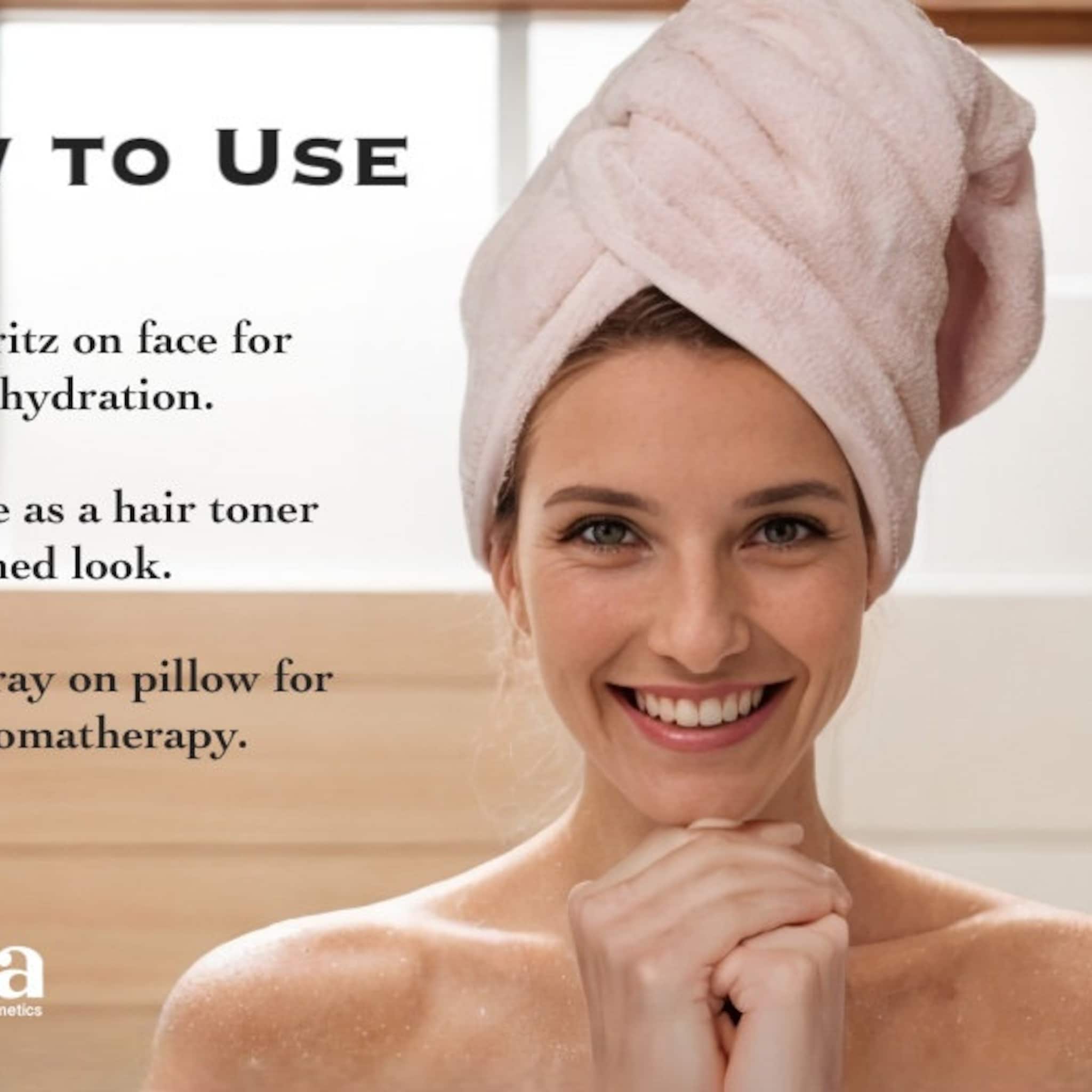 Woman wearing pink towel on head, smiling, with hands under chin, for skincare use