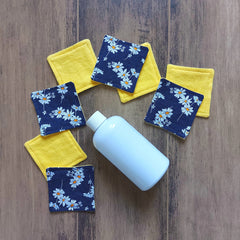 Makeup remover pads, yellow and daisy print fabric, with a white bottle on wood surface