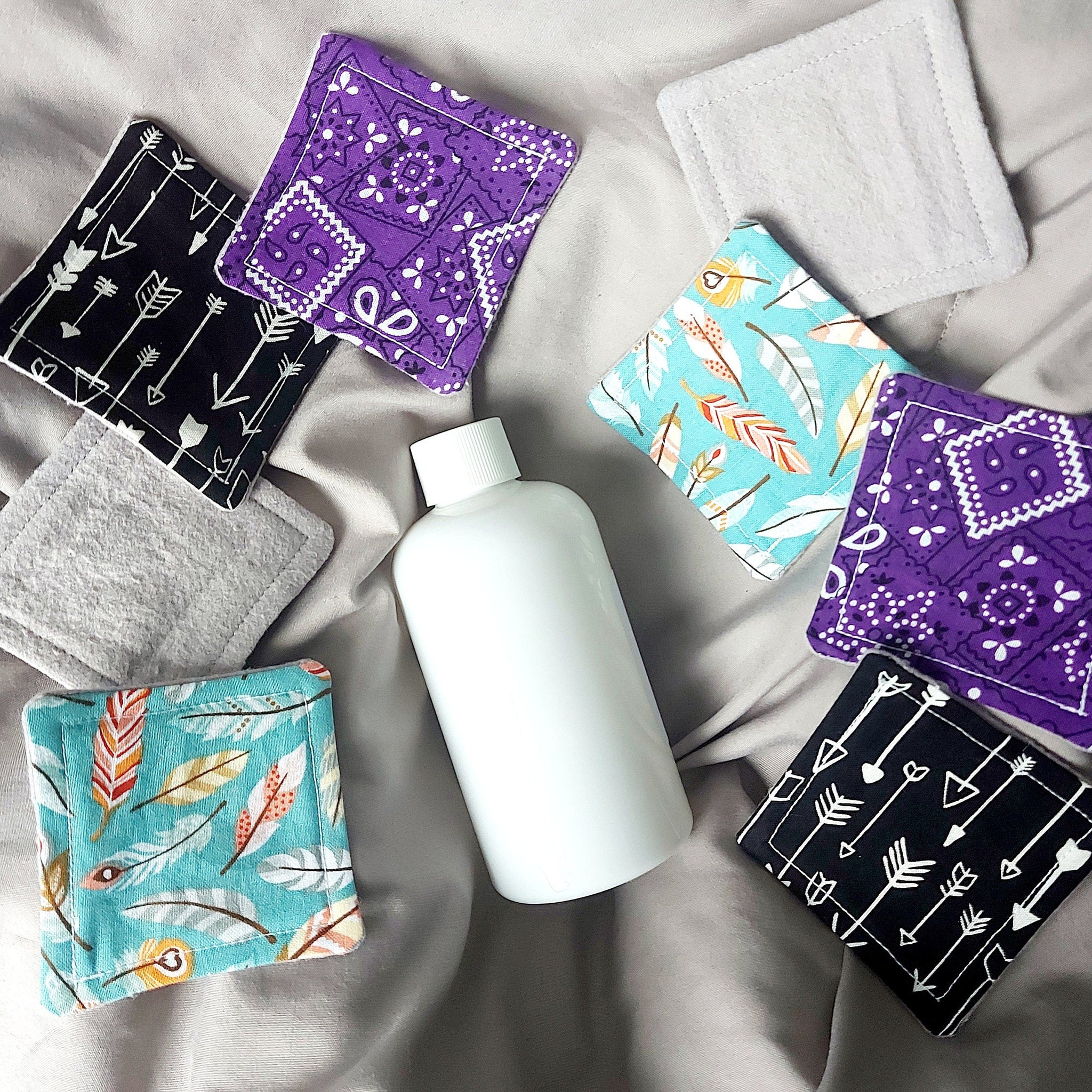 Makeup remover pads with arrow and feather patterns, various colors, and white bottle