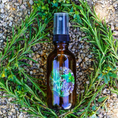 Skin care garden mist bottle, brown glass, black cap, surrounded by green rosemary and purslane