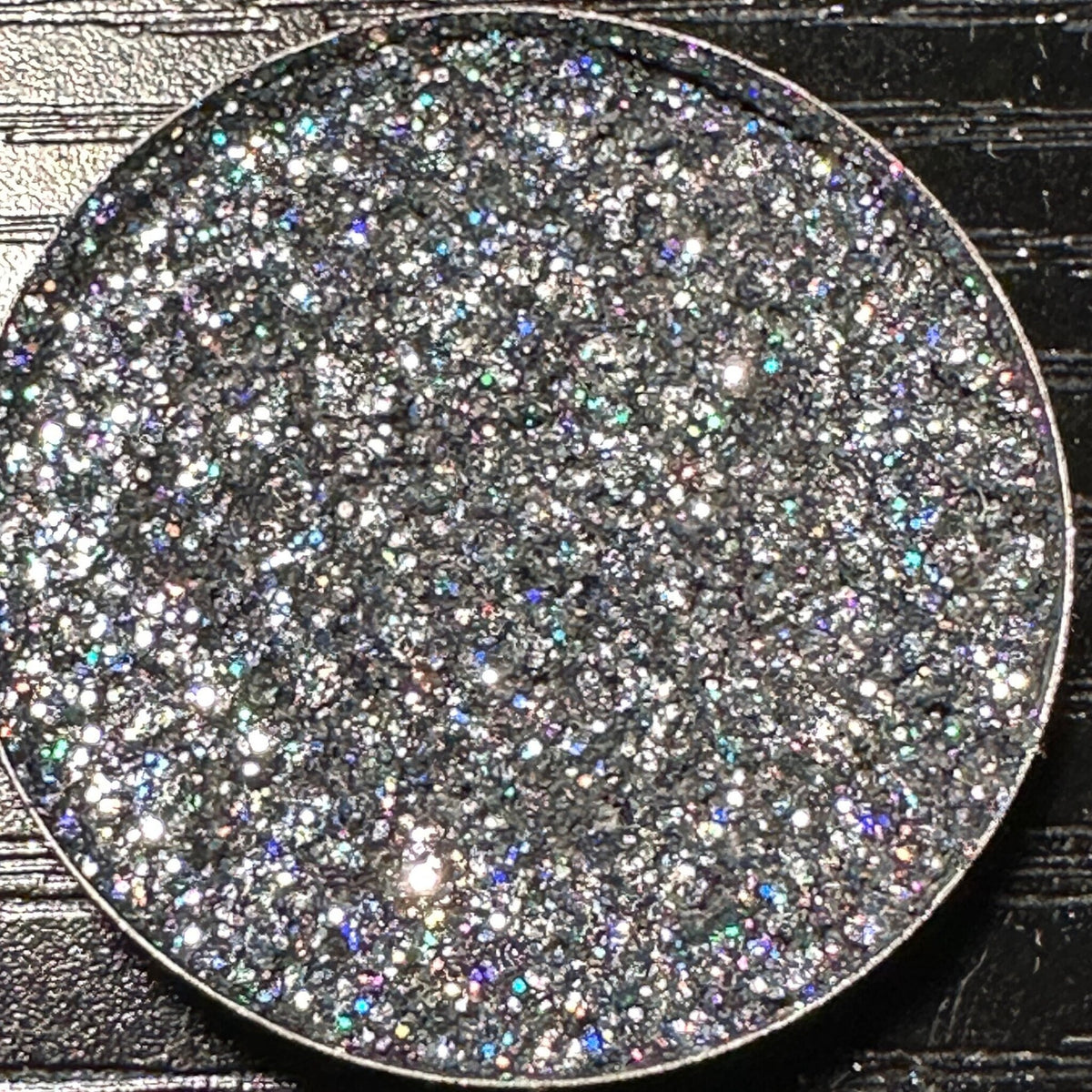 Close-up of dark gray holographic glitter eyeshadow in a round 26mm metal pan with reflective sparkles
