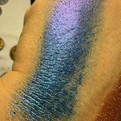 Side angle view of dark blue duochrome pressed glitter eyeshadow pan showing shimmer shift in light