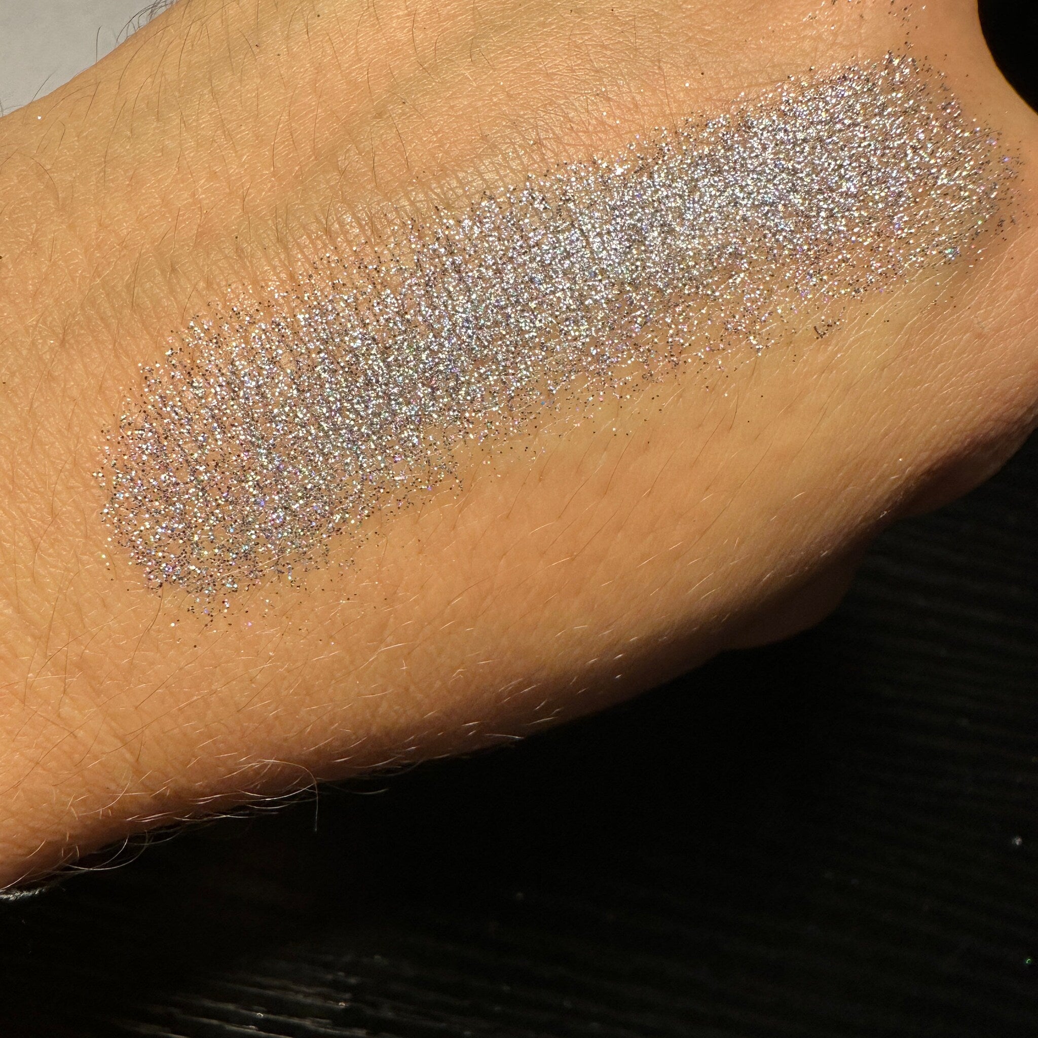Close-up of black pressed glitter eyeshadow with holographic sparkle in a 26mm pan
