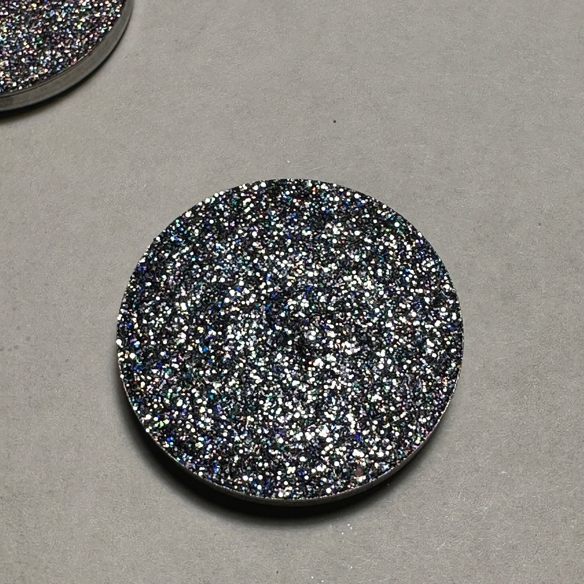 Close-up of a fingertip applying black holo pressed glitter eyeshadow with sparkling reflective particles.