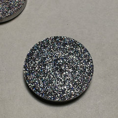 Close-up of a fingertip applying black holo pressed glitter eyeshadow with sparkling reflective particles.