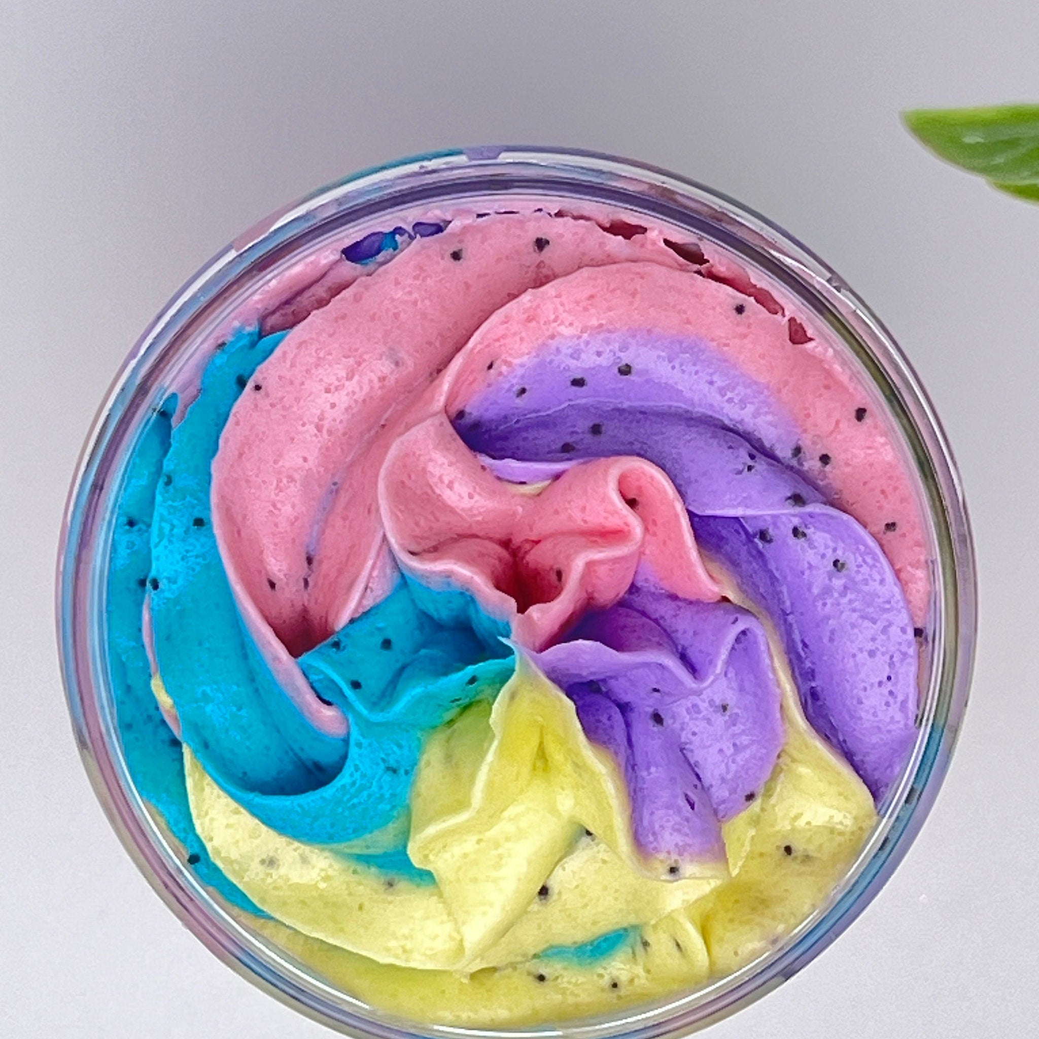 Whipped soap with pink, blue, yellow, and purple swirls, black specks, in a clear container