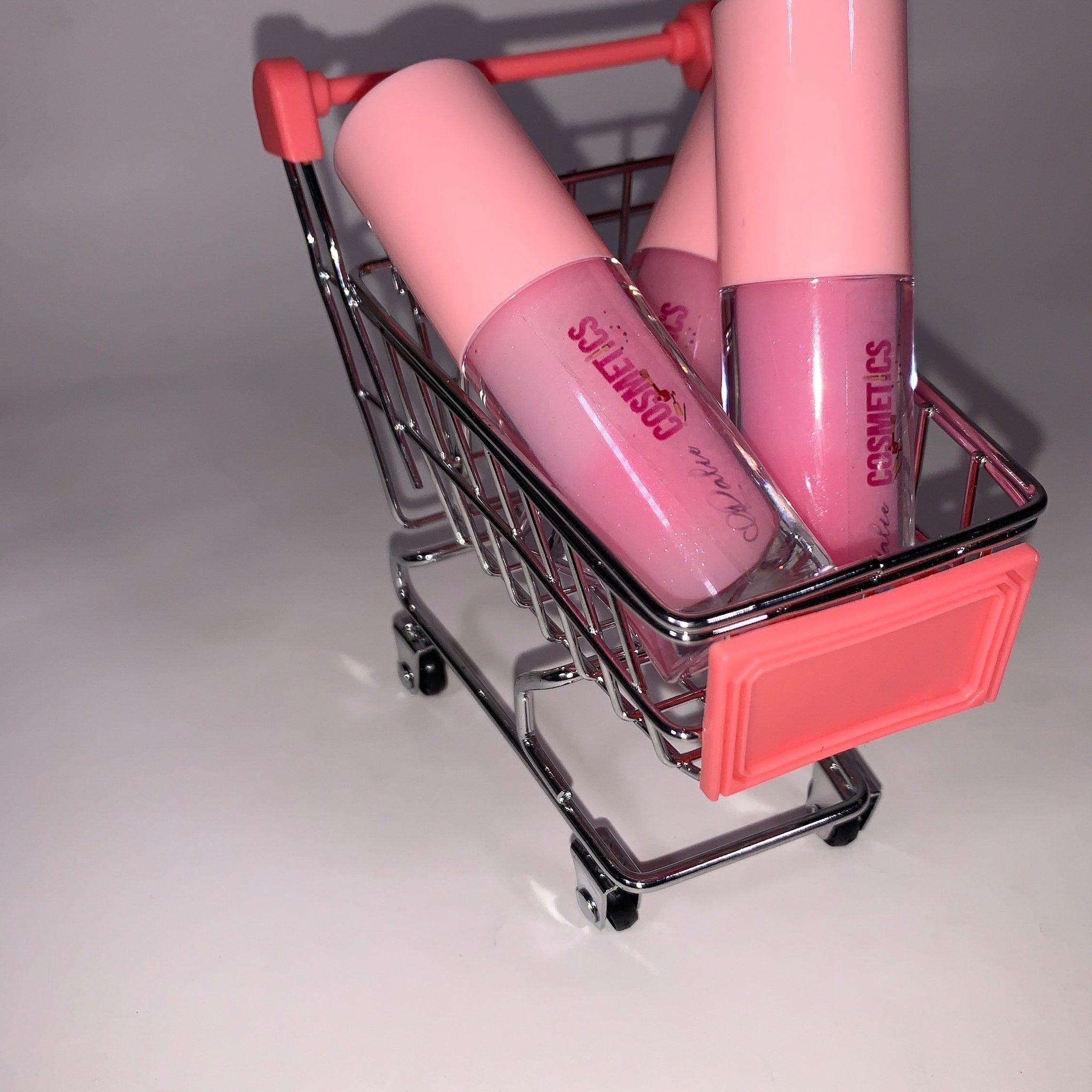 Lip balms in pink tubes and glass bottles, in a miniature shopping cart, Pinky Cosmetics visible