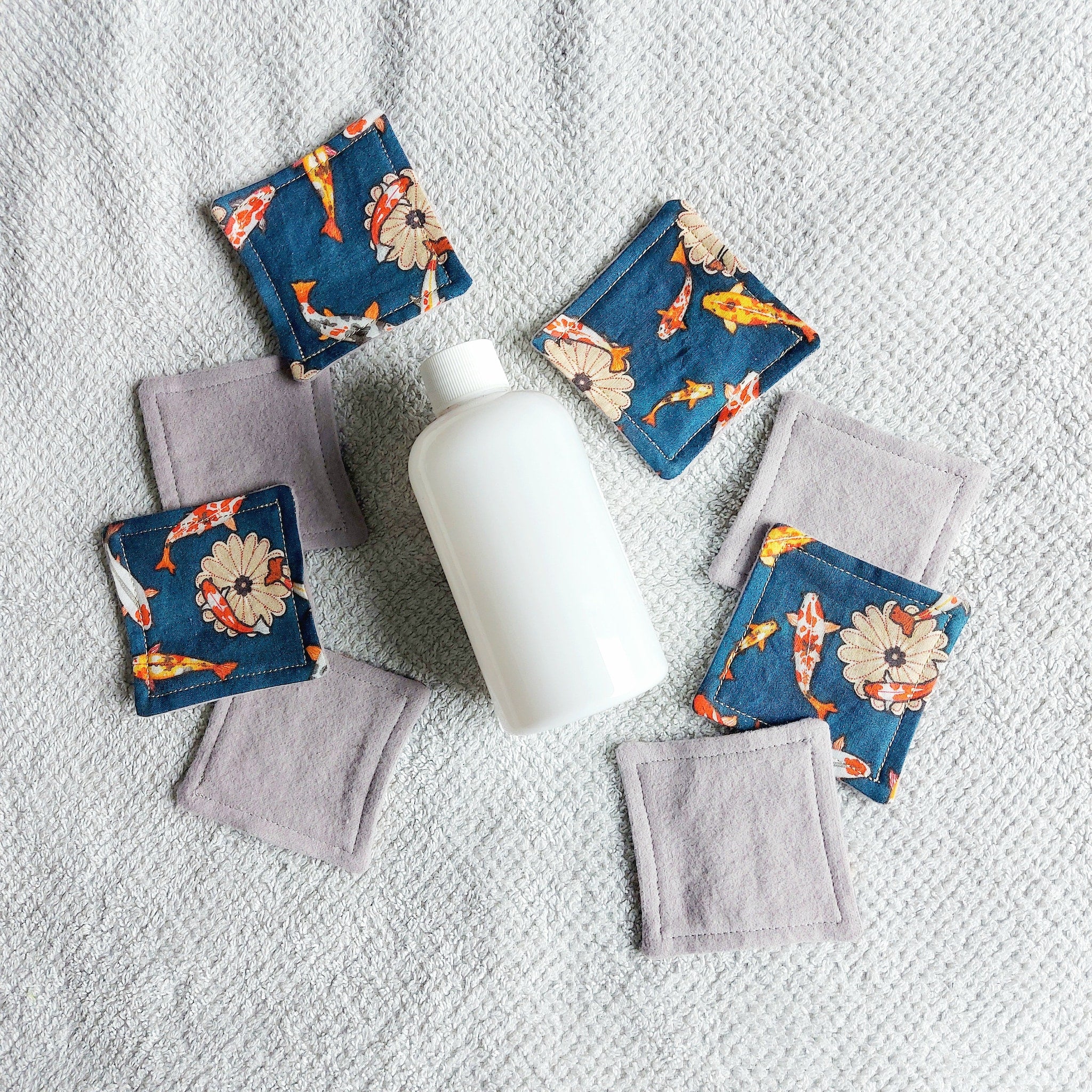 Reusable face pads with koi fish pattern and gray fabric, near white bottle